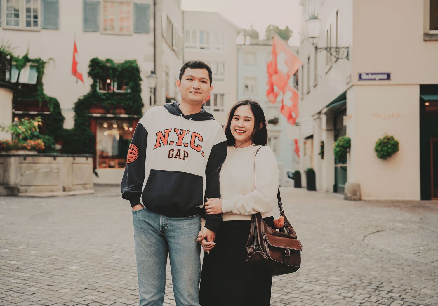 Asian couple posing together on a cobblestone street in Zurich old town with Swiss flags.