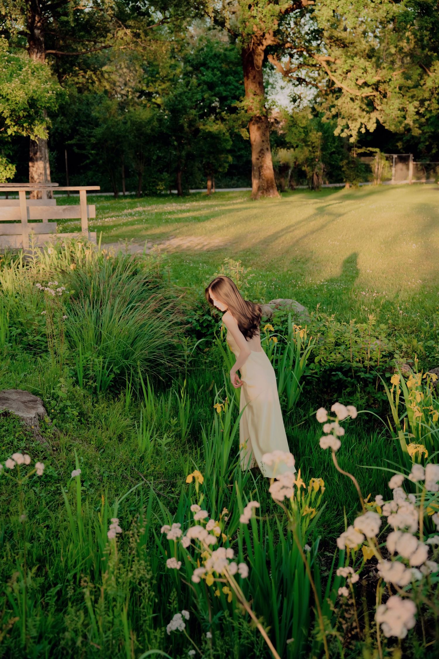 Woman in flowing pale yellow dress tossing hair among wildflowers in a golden hour garden setting.