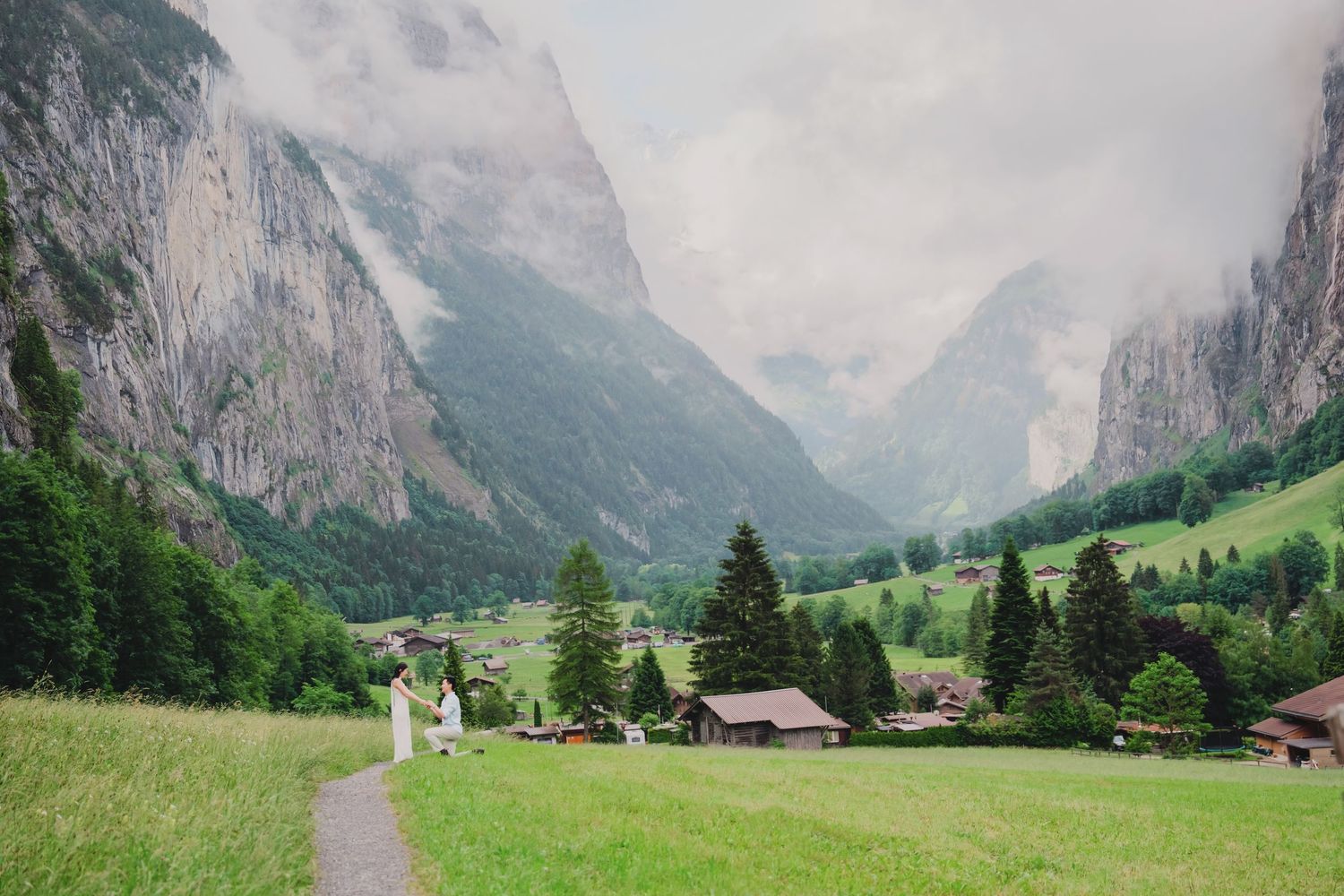 Couple walking on a path through lush Lauterbrunnen valley with dramatic Swiss Alps cliffs and green meadows.