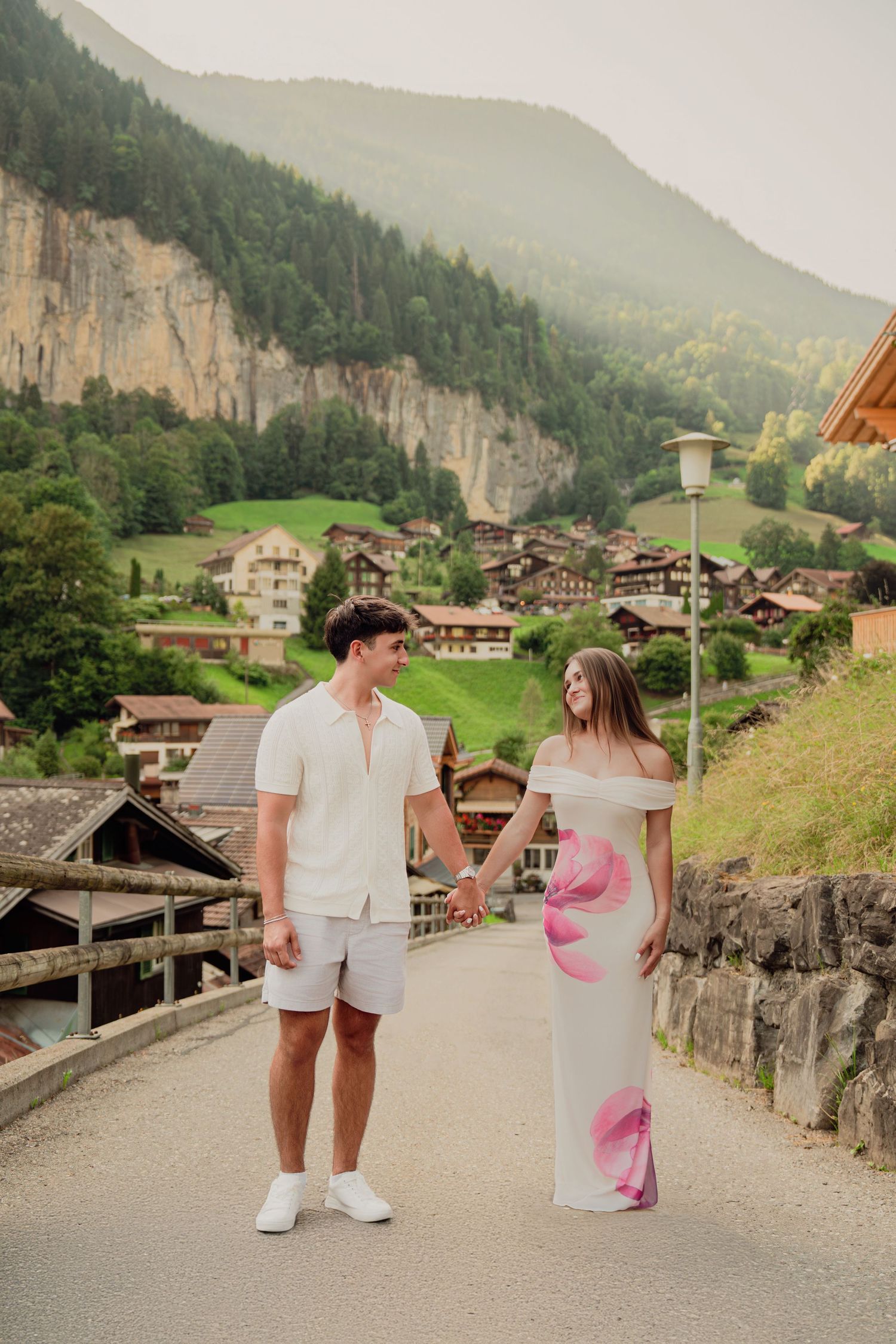 Couple holding hands and smiling on a road in Lauterbrunnen with Swiss chalets and mountains behind.