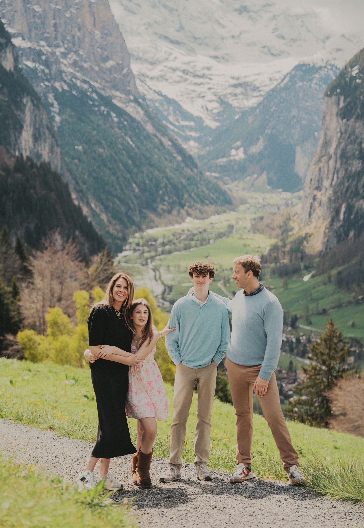Family of four laughing together on a mountain path with Lauterbrunnen valley backdrop.