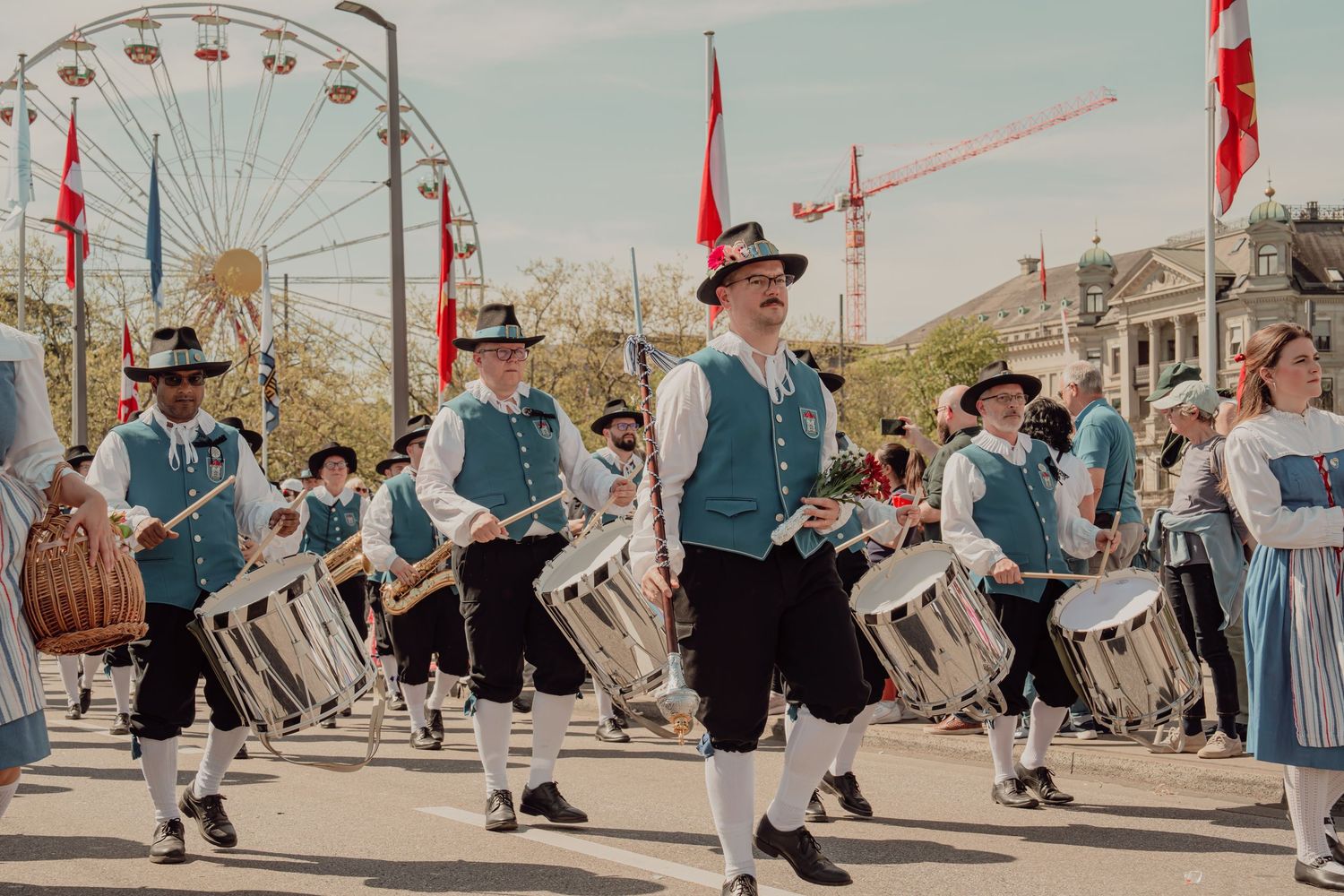 Traditional Swiss marching band in folk costumes playing drums at an outdoor spring parade.