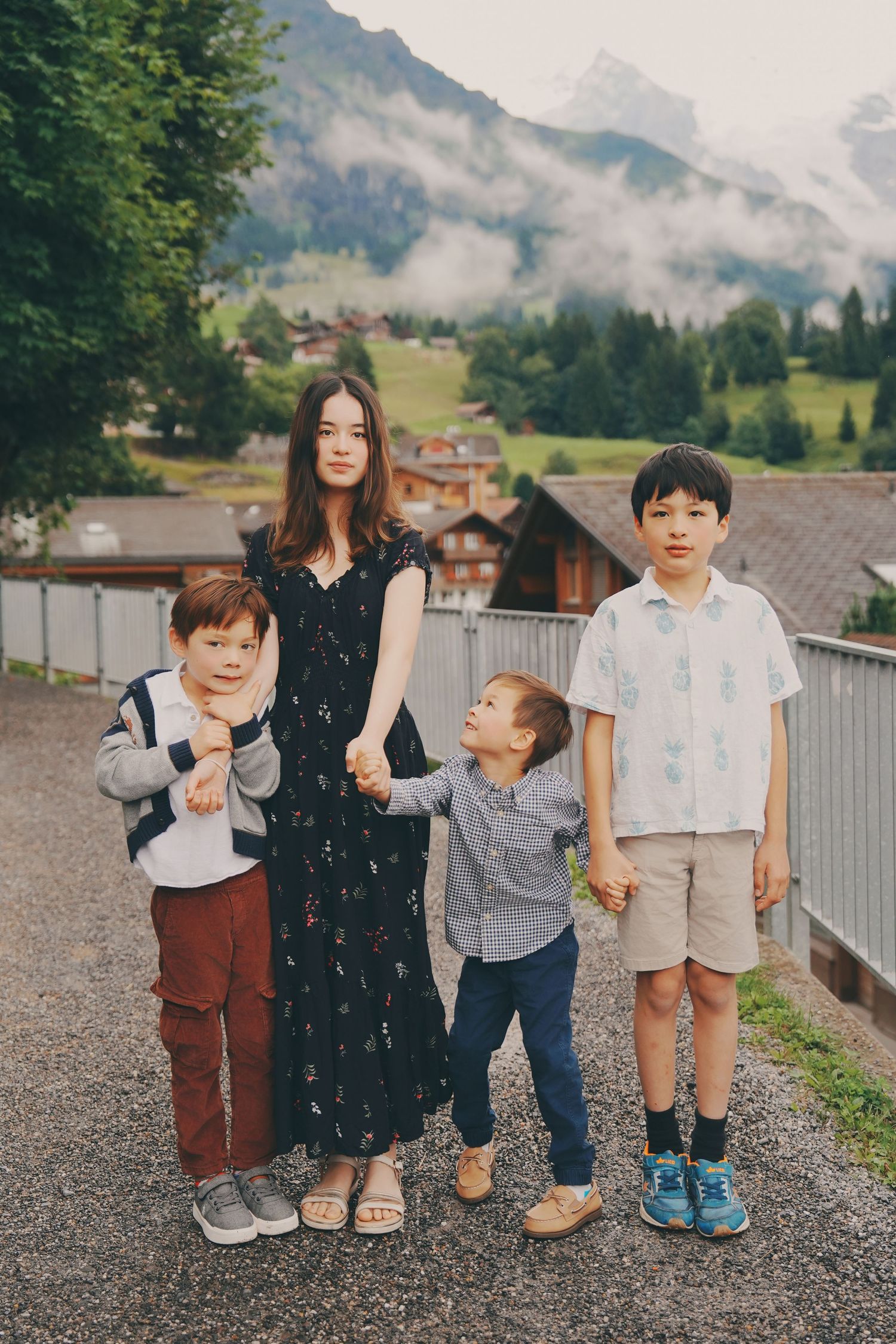 A teenage girl stands with three young boys on a path overlooking a misty Swiss alpine village.
