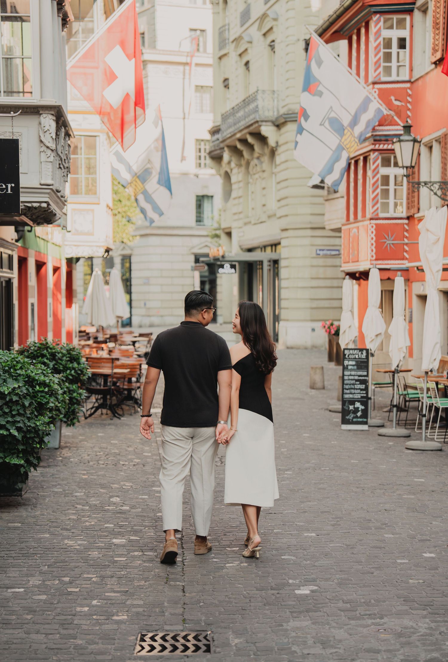 Couple strolling hand in hand down a Swiss old town street adorned with colorful flags and buildings.