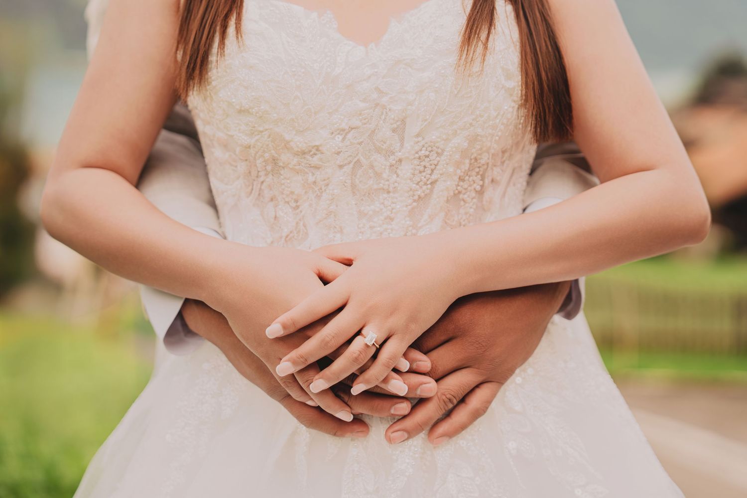 Close-up of bride and groom hands intertwined showing elegant diamond engagement ring on wedding day.
