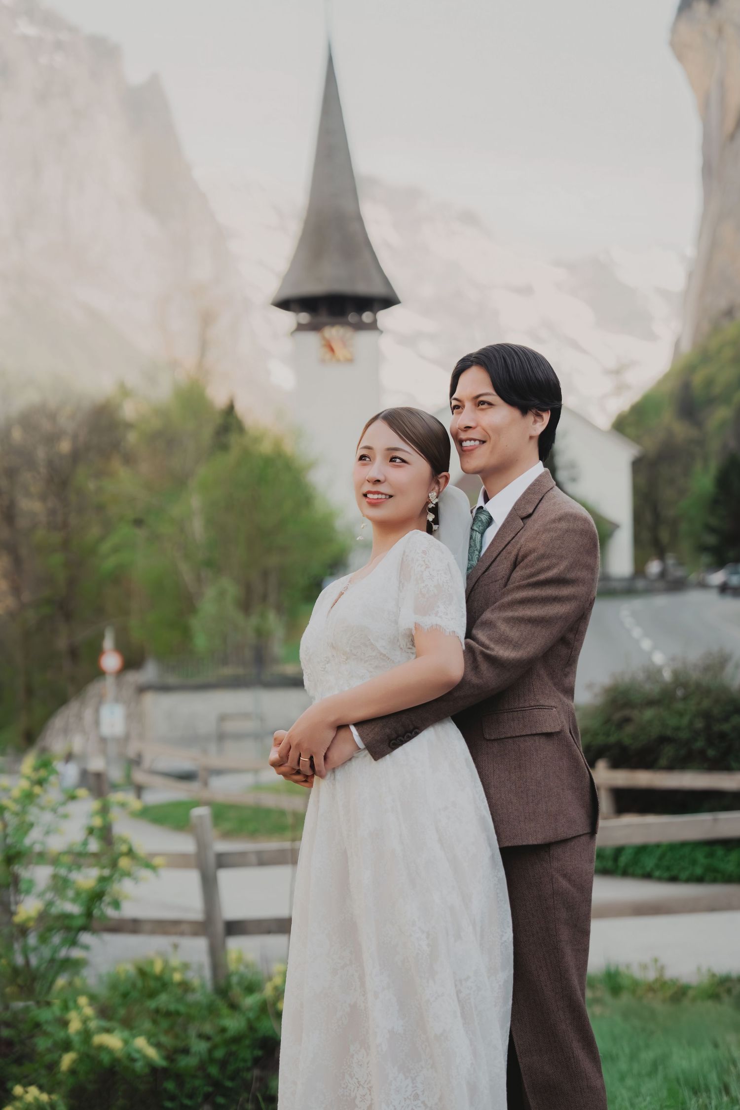 Bride and groom smiling together with a Swiss alpine church steeple and mountains in the background.