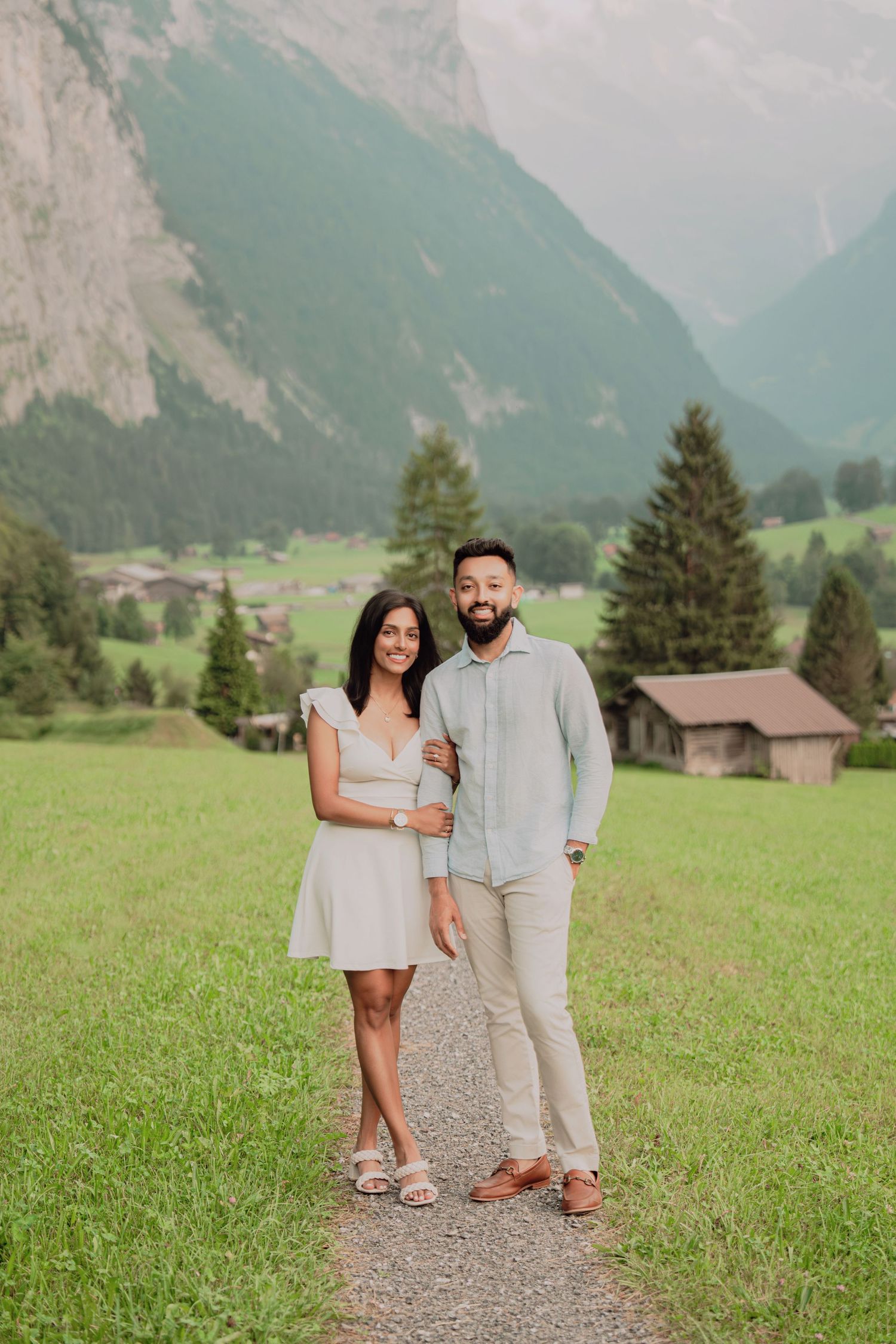Smiling engaged couple standing together on a gravel path in a stunning Swiss mountain valley.