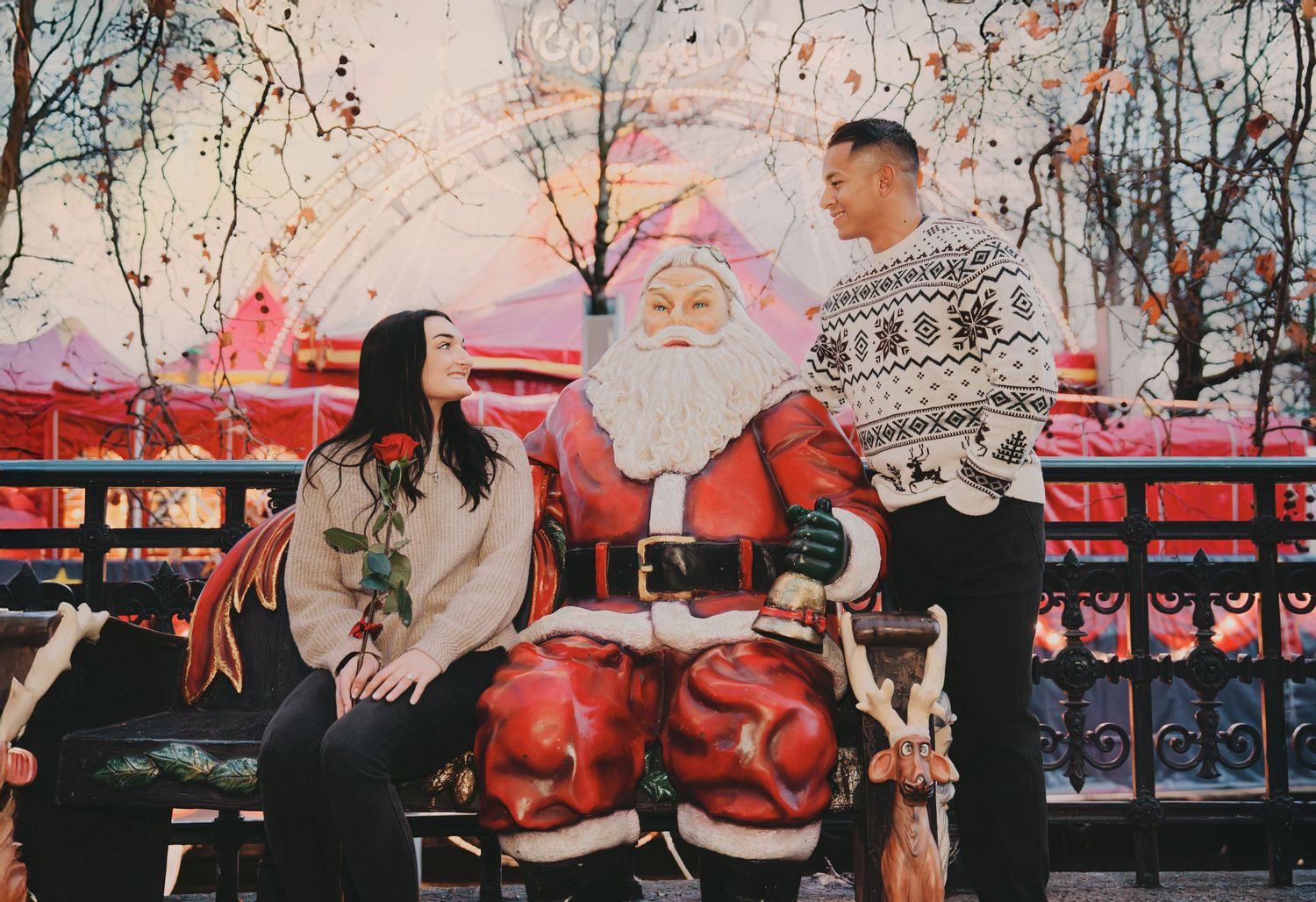 Couple posing with Santa Claus at a festive Christmas market with colorful holiday decorations.