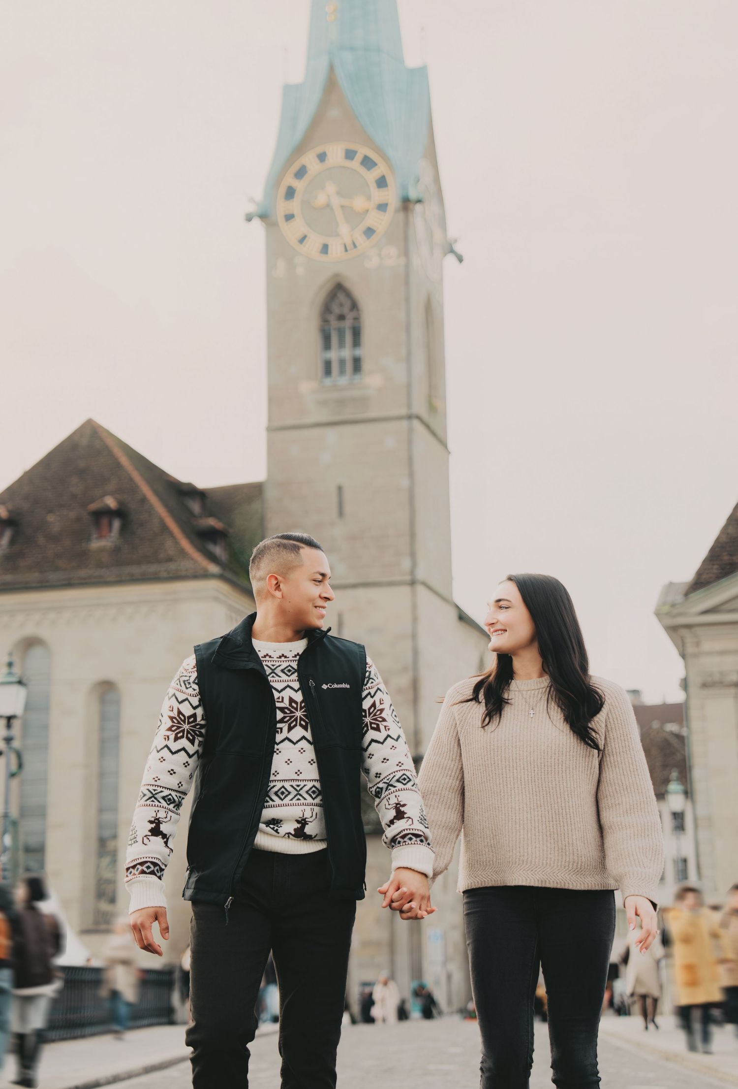 Happy couple walking hand in hand past Fraumunster Church clock tower in Zurich, Switzerland.