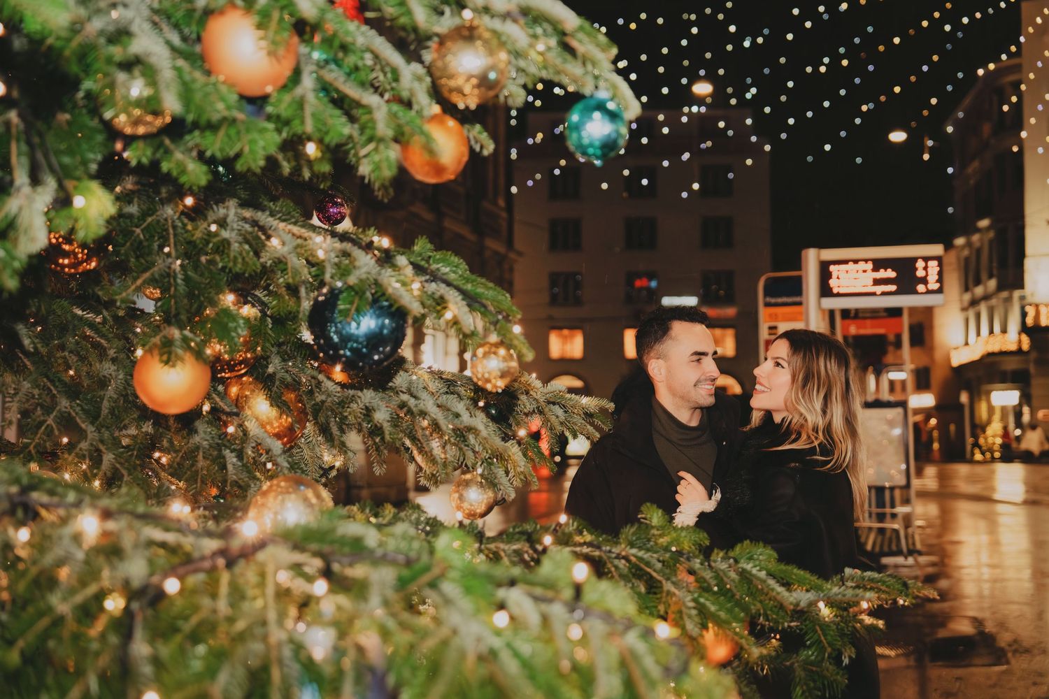 Couple sharing a tender moment beside a decorated Christmas tree with golden ornaments.