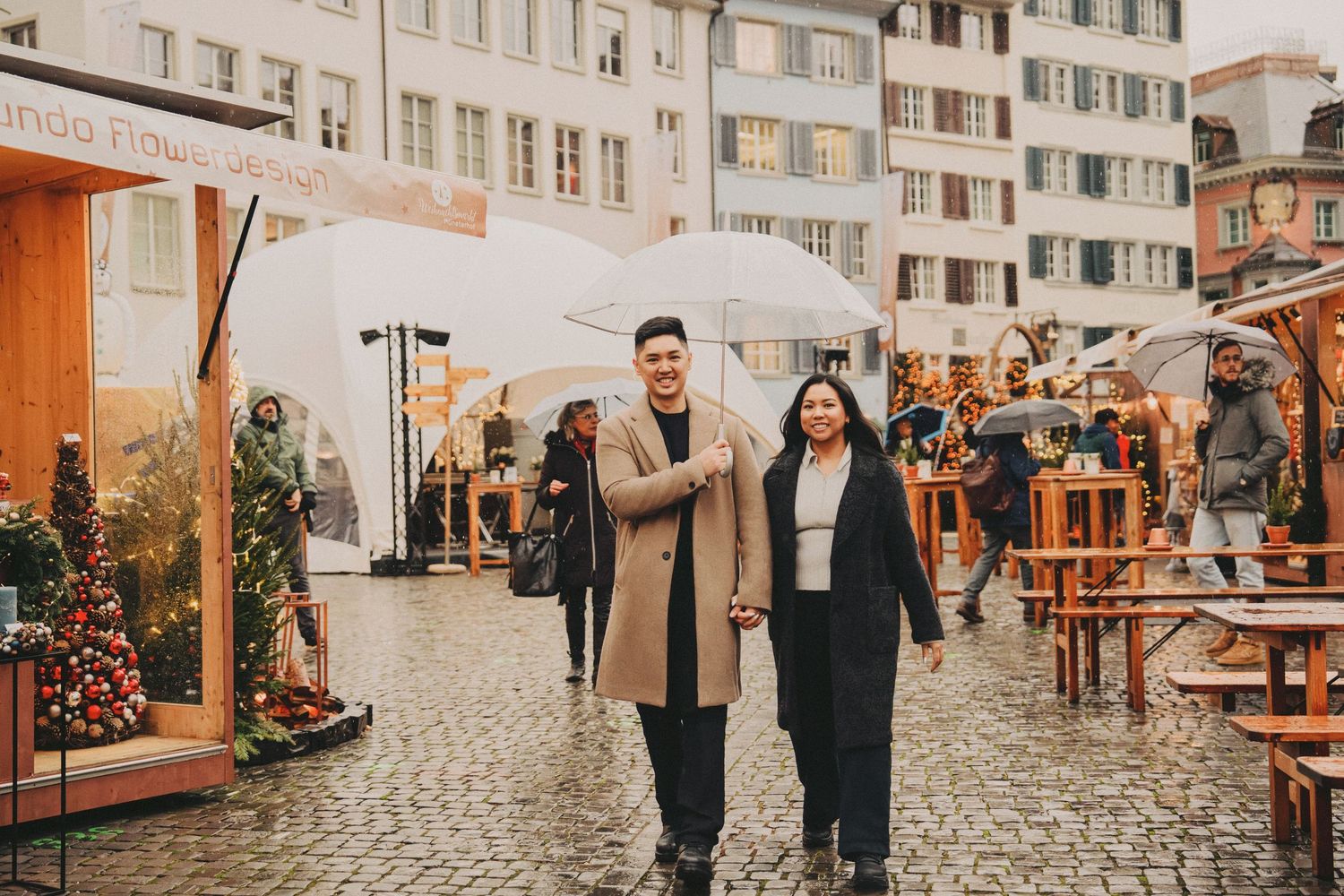 Couple walking hand in hand through rainy Christmas market cobblestone square.