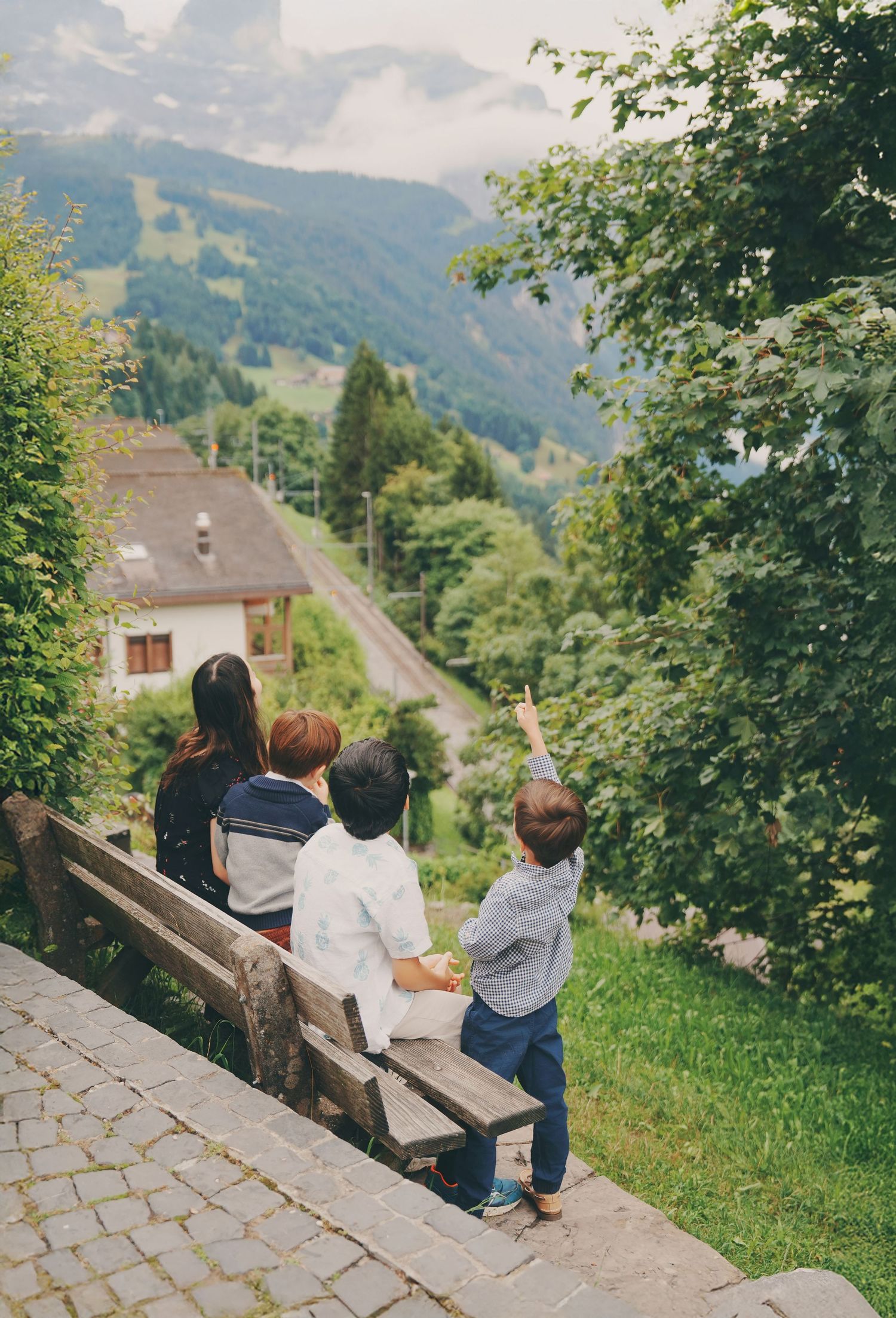 A woman and three children sit on a bench admiring the stunning Swiss mountain valley view.