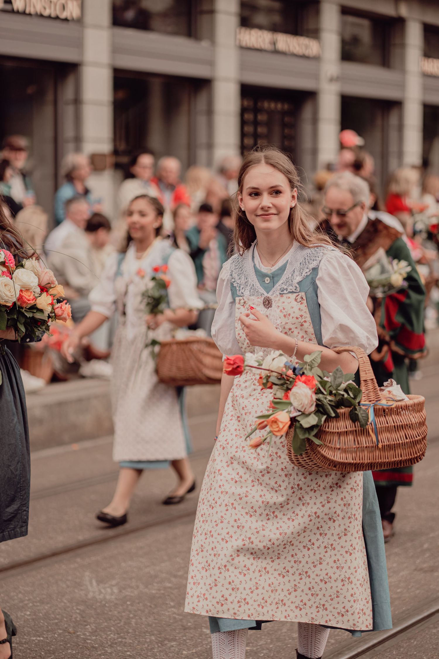 Smiling young woman in traditional folk apron carries a wicker basket of colorful flowers in parade.