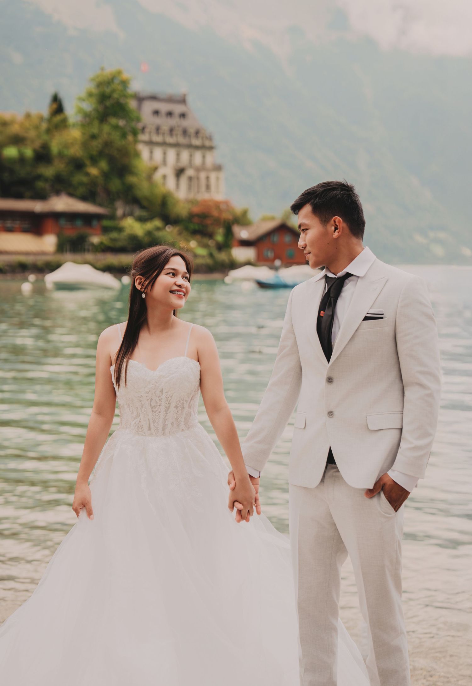 Wedding couple holding hands and gazing at each other by a beautiful alpine lake with mountain scenery.