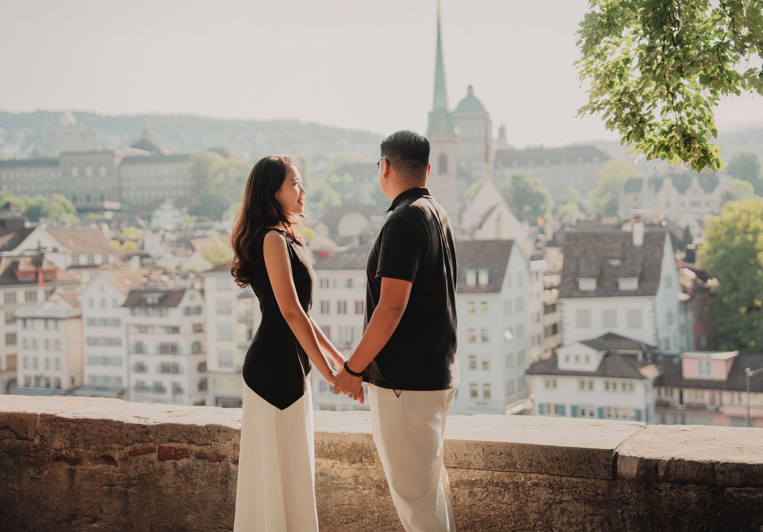 Couple holding hands facing each other with the Zurich old town skyline and church spire in the background.