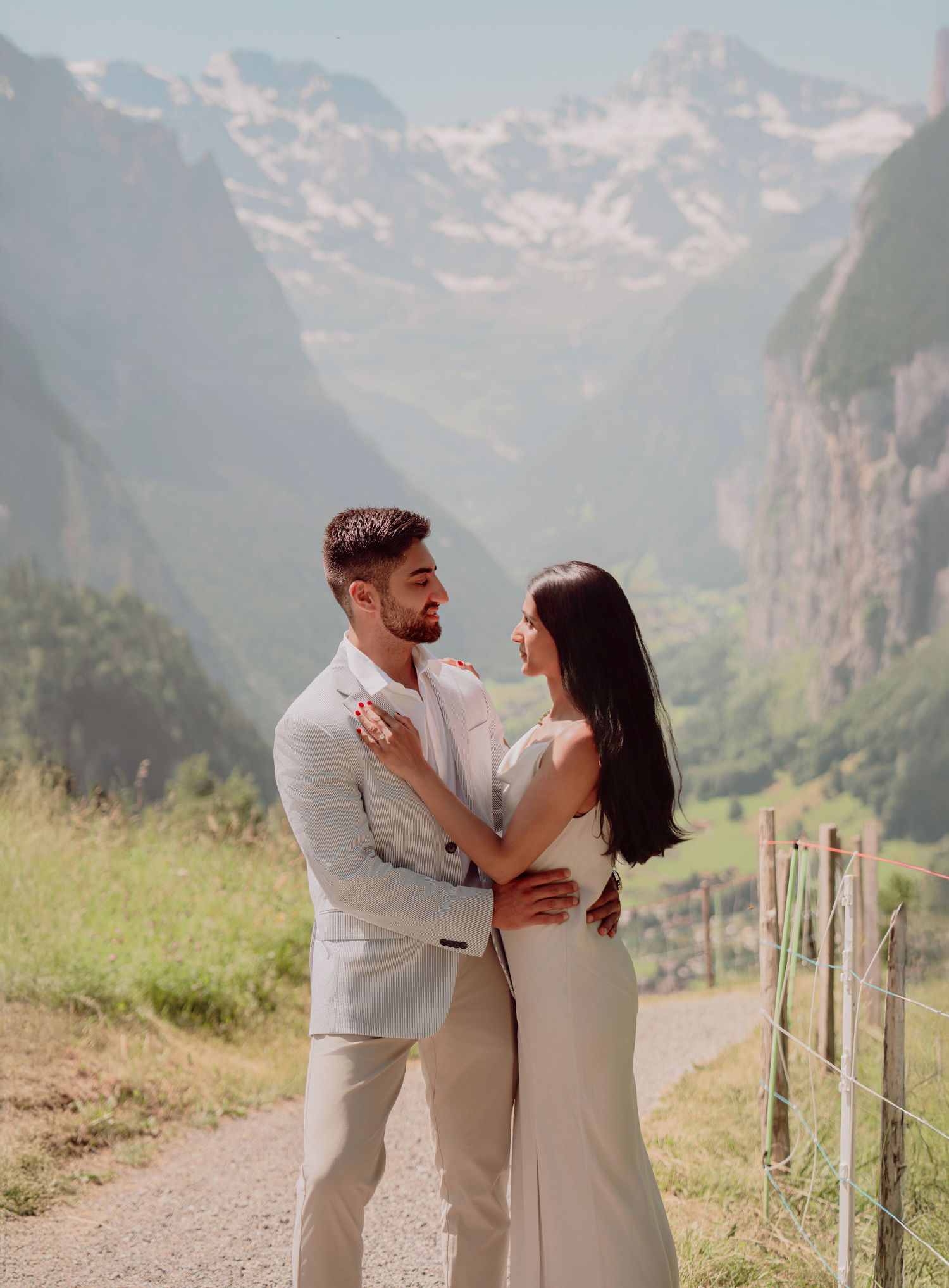 Romantic couple in wedding attire embracing on a mountain path with stunning Swiss Alps valley view.