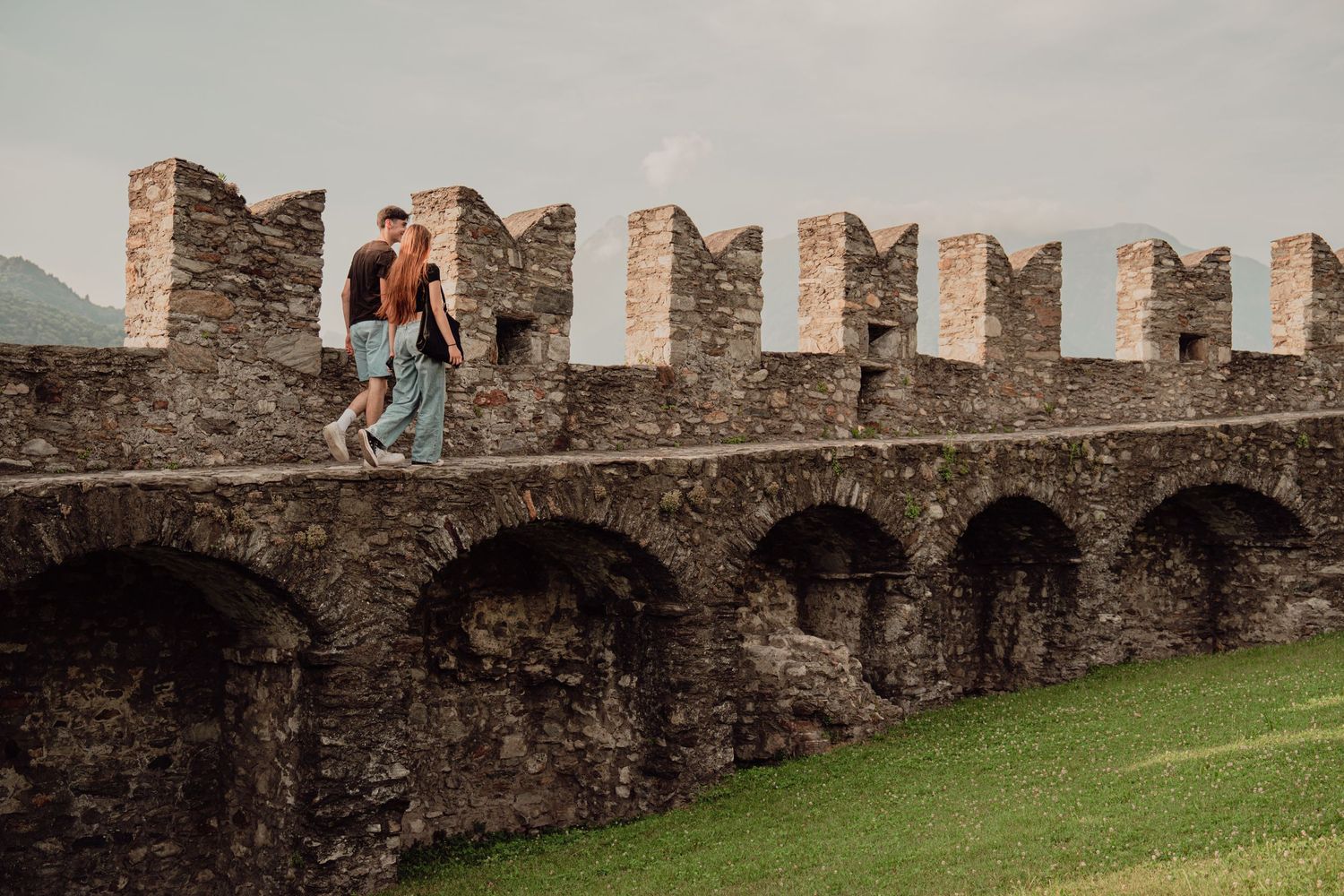 Young couple strolling together on historic medieval stone fortress wall with crenellations.