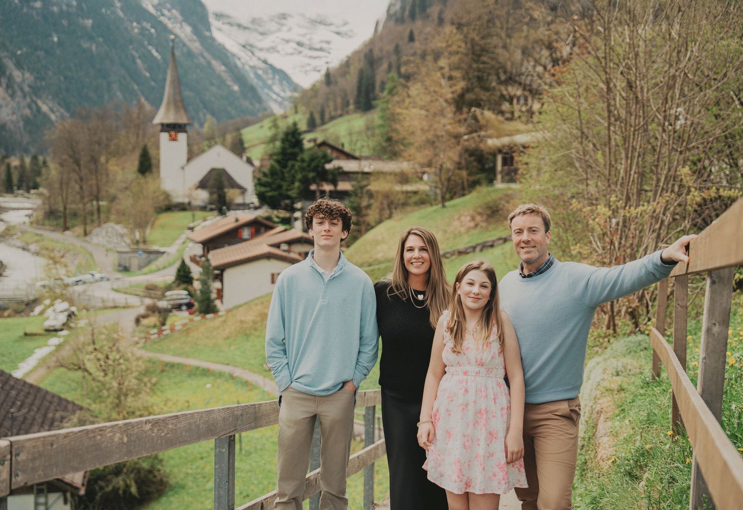 Family of four posing on a wooden bridge with a beautiful Swiss Alpine village backdrop.