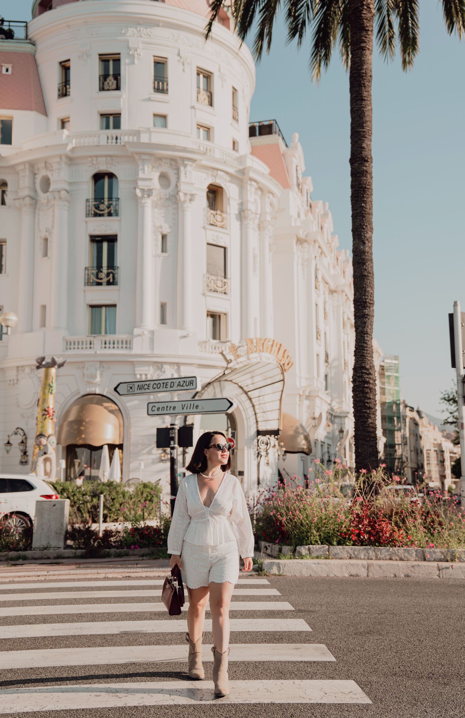 Woman in white romper taking selfie near Le Negresco hotel on Nice Promenade des Anglais.