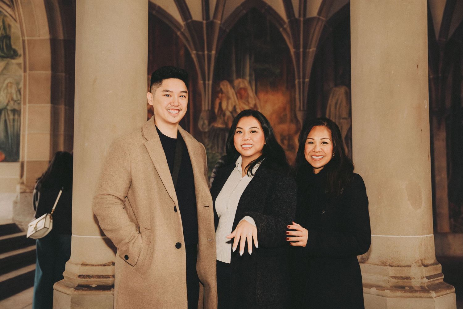 Three people standing together and smiling inside a cathedral with gothic arched columns.
