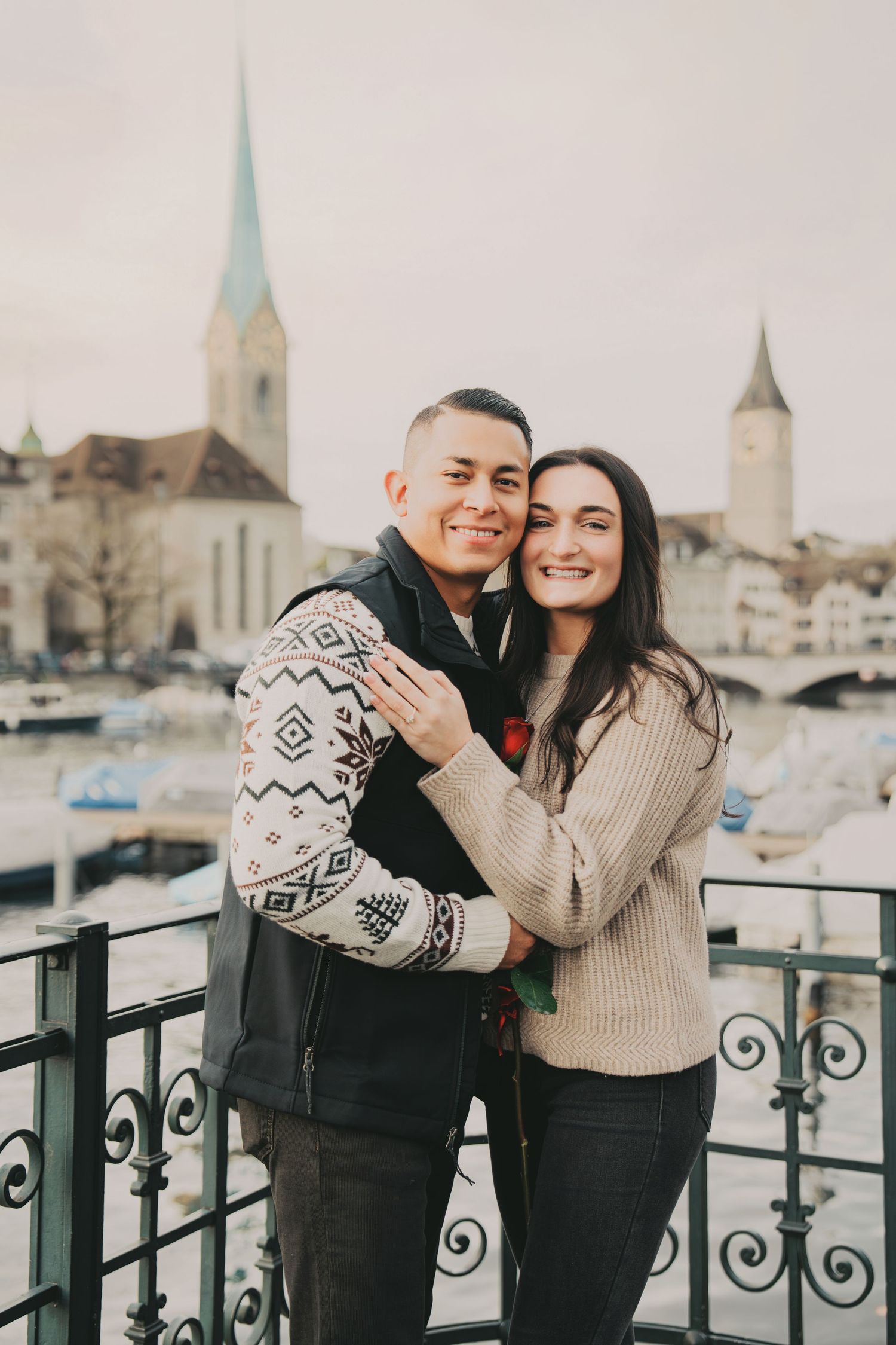 Joyful couple hugging on balcony with scenic Zurich cityscape and river backdrop.