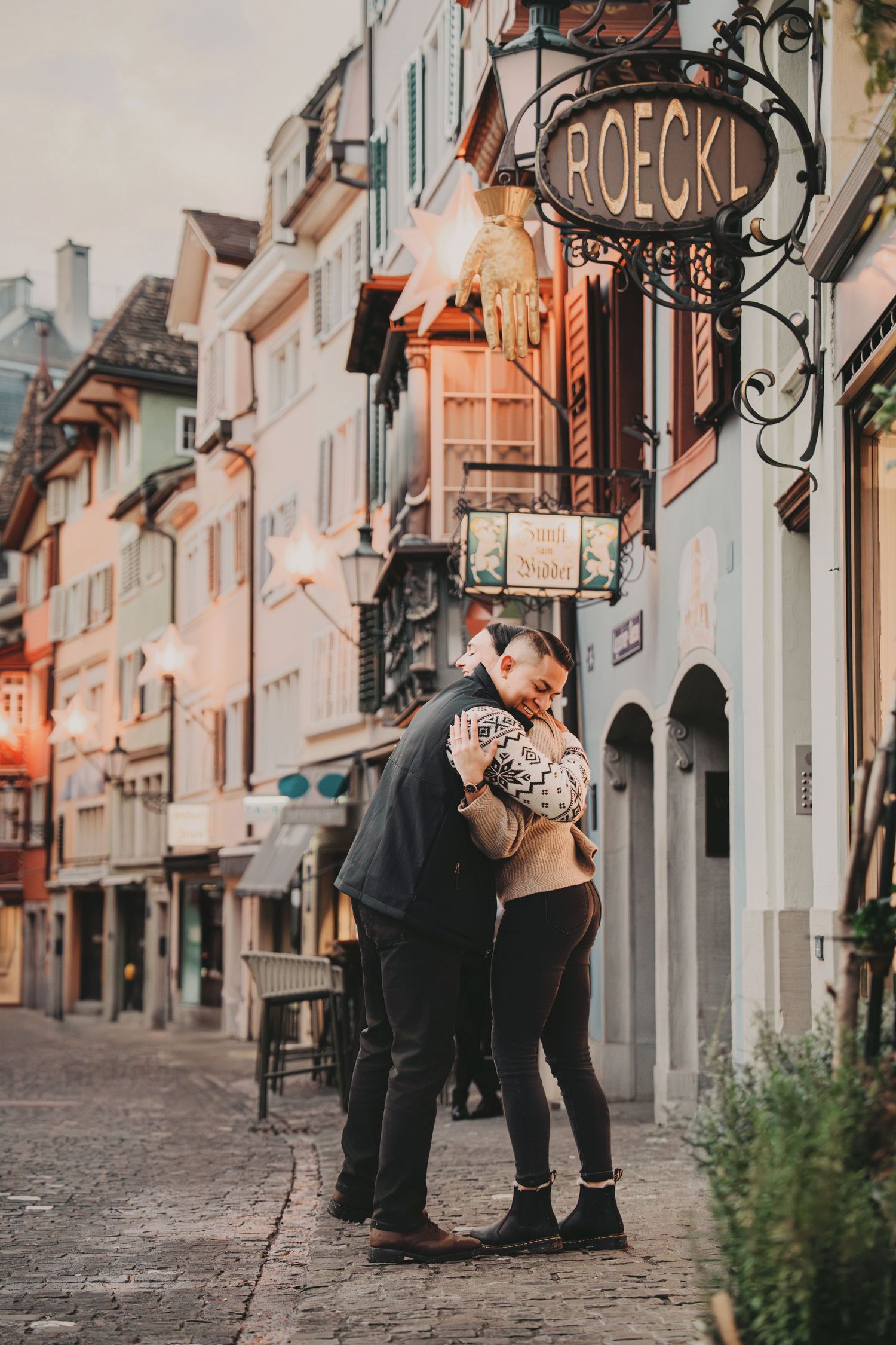 Couple sharing a tender embrace on a charming European cobblestone street at dusk.