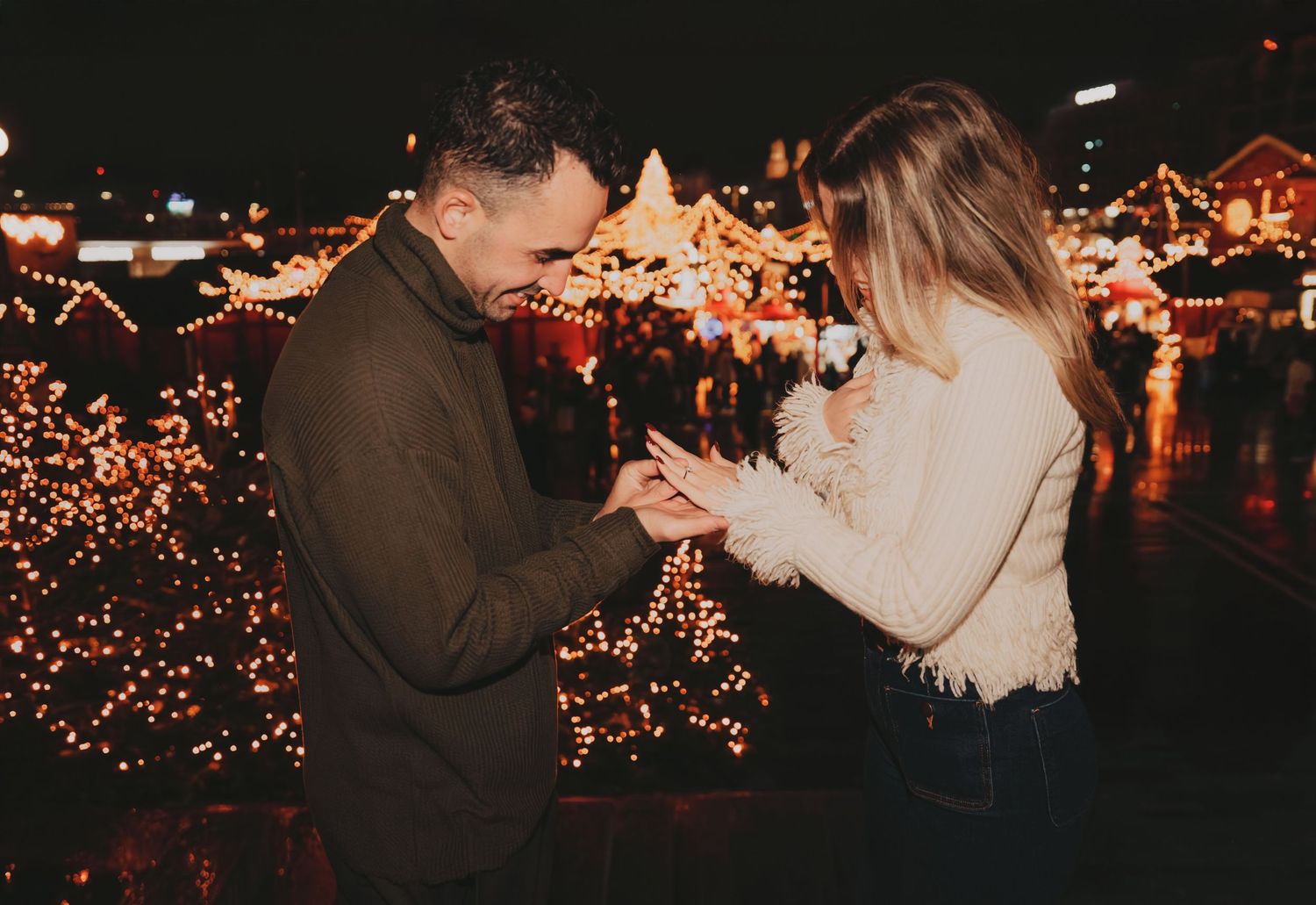Man proposing to woman at a magical Christmas market with glowing holiday lights in the background.