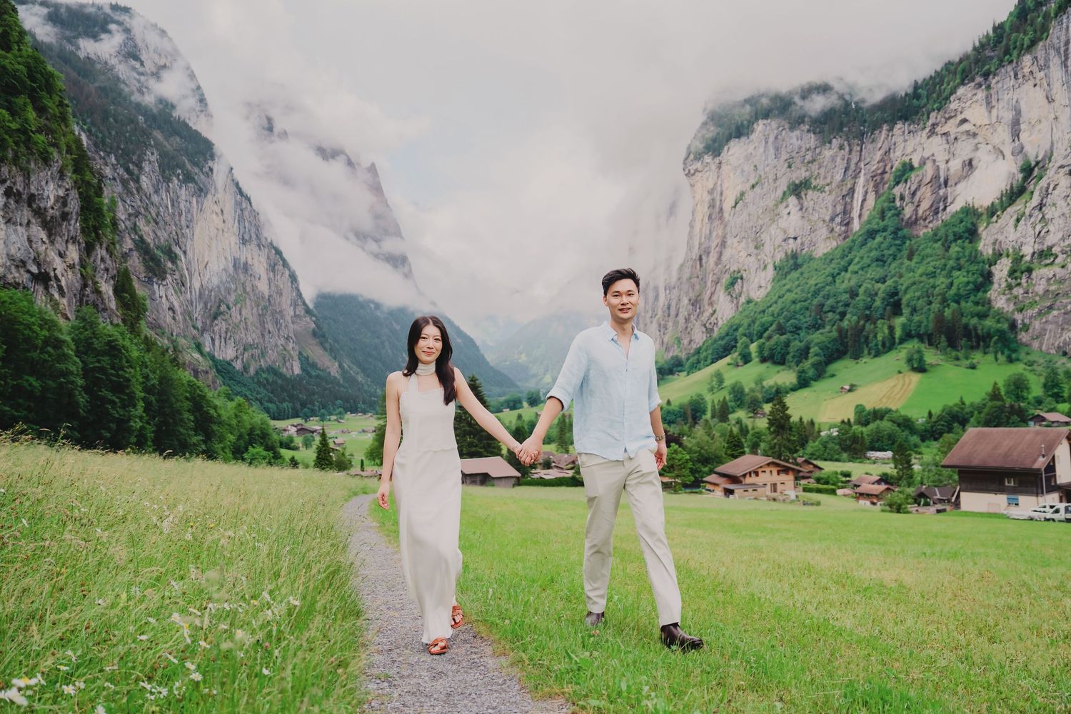 Couple walking hand in hand through a lush Swiss alpine valley with towering rocky mountains.
