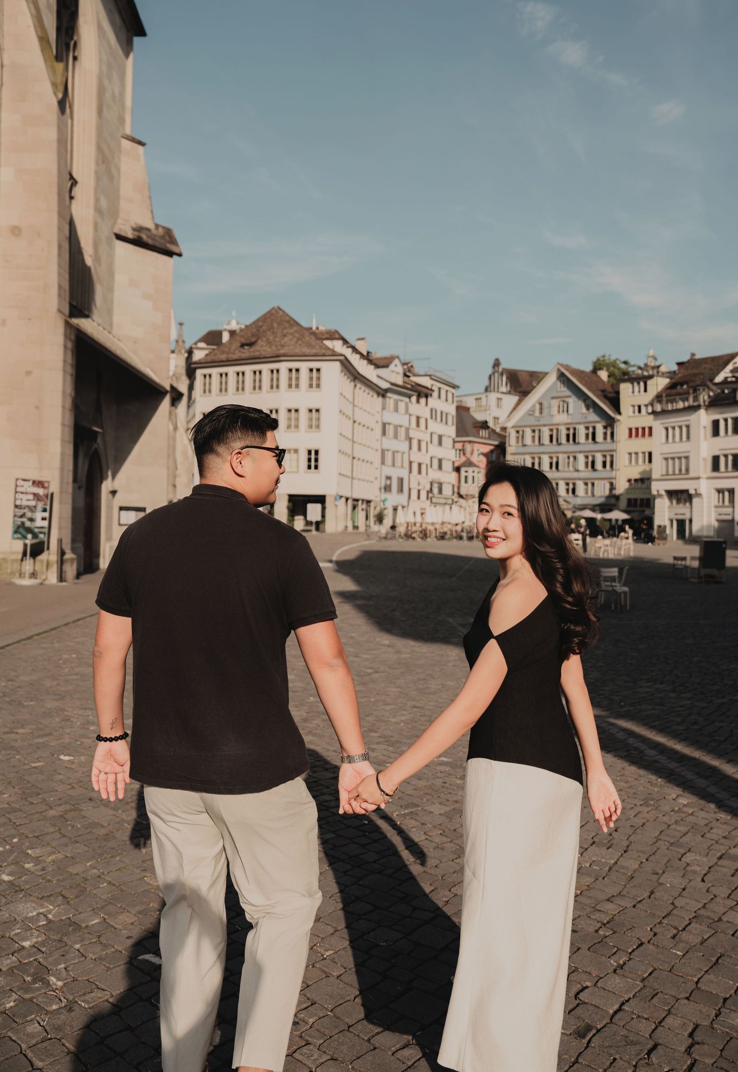 Woman smiling back at camera while holding hands with partner in Zurich cobblestone square.