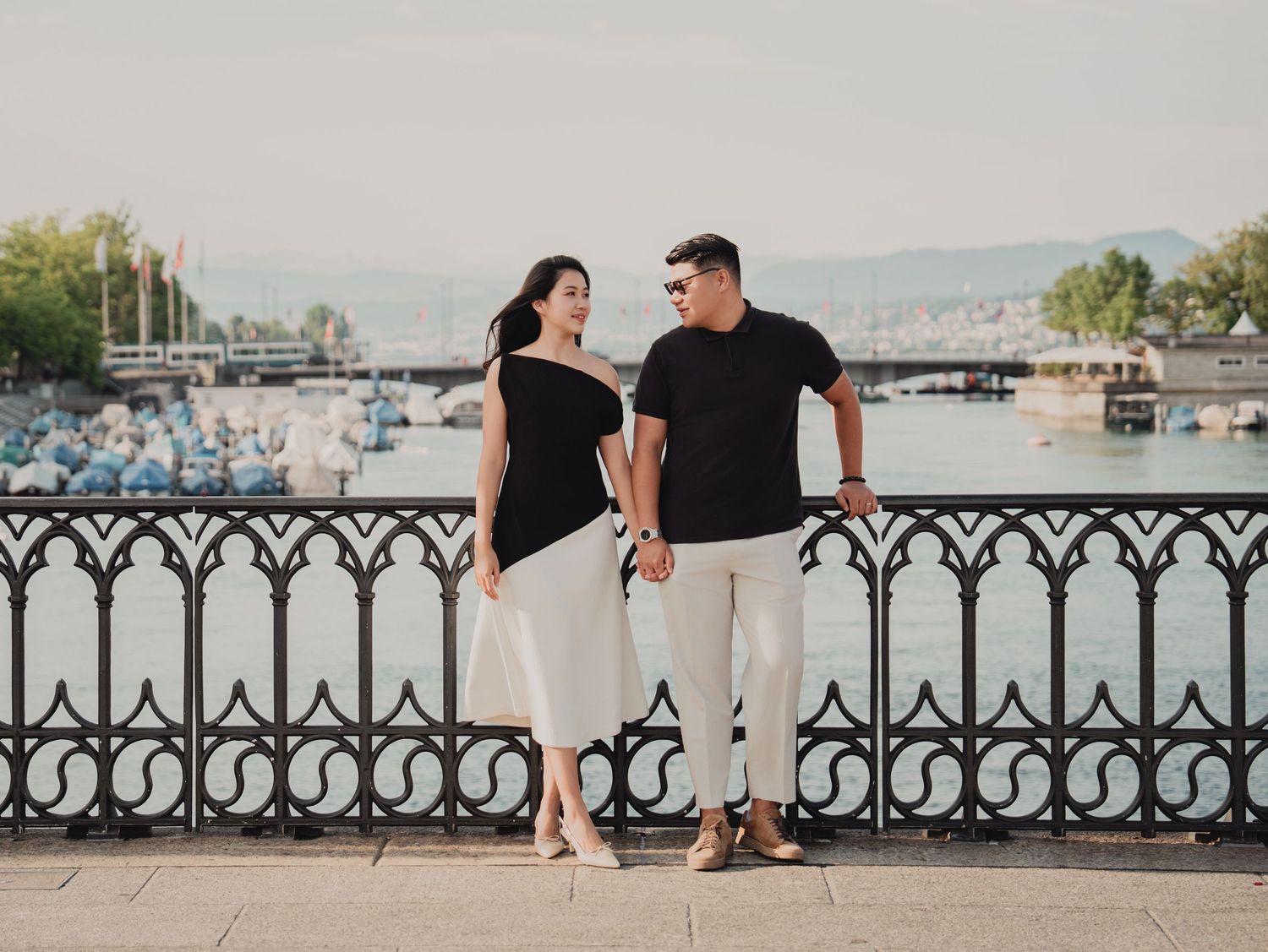 Young couple walking hand in hand along scenic Zurich lakefront with decorative iron fence.