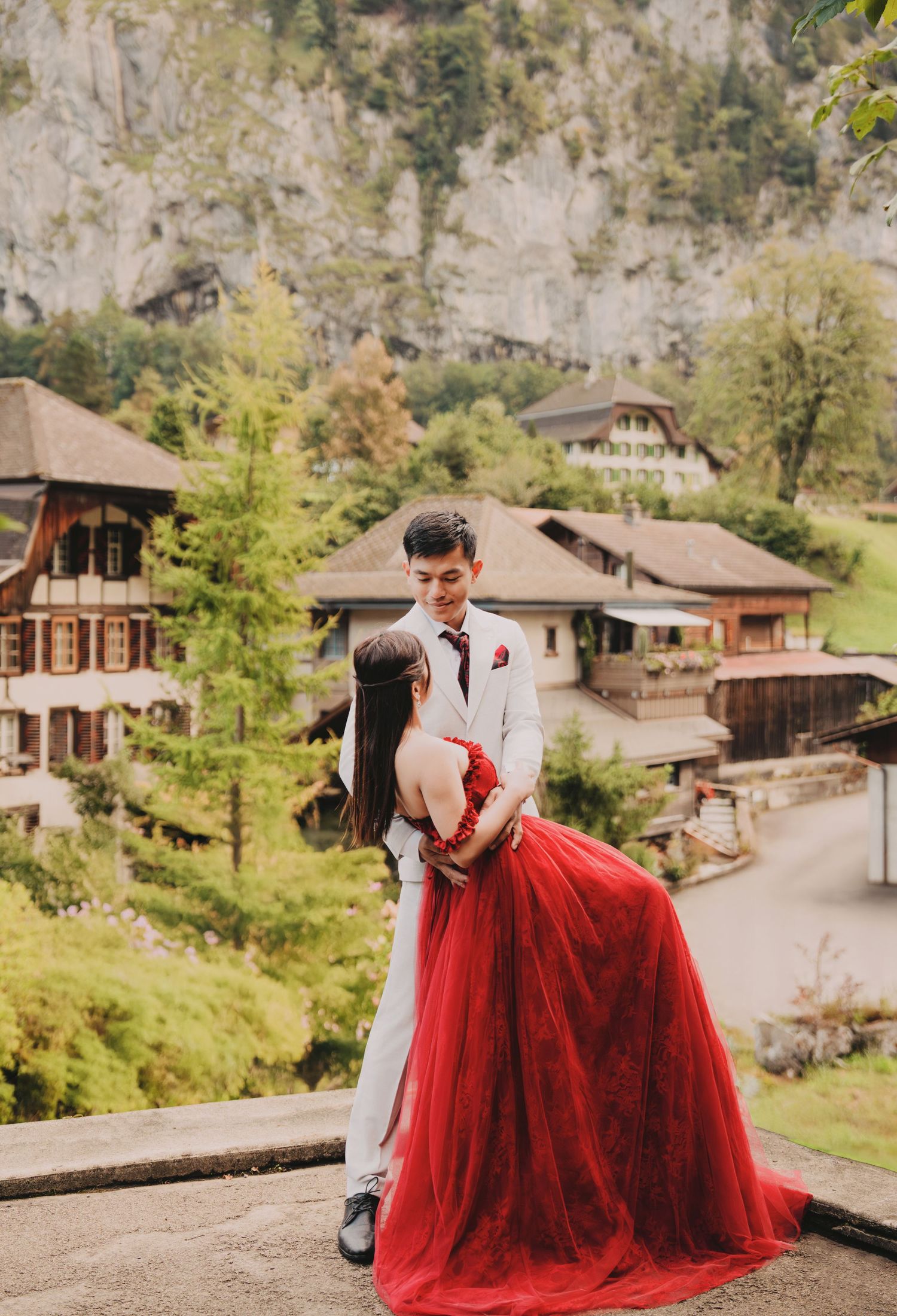 Groom dips bride in stunning red dress during romantic pre-wedding shoot in Swiss mountain village.