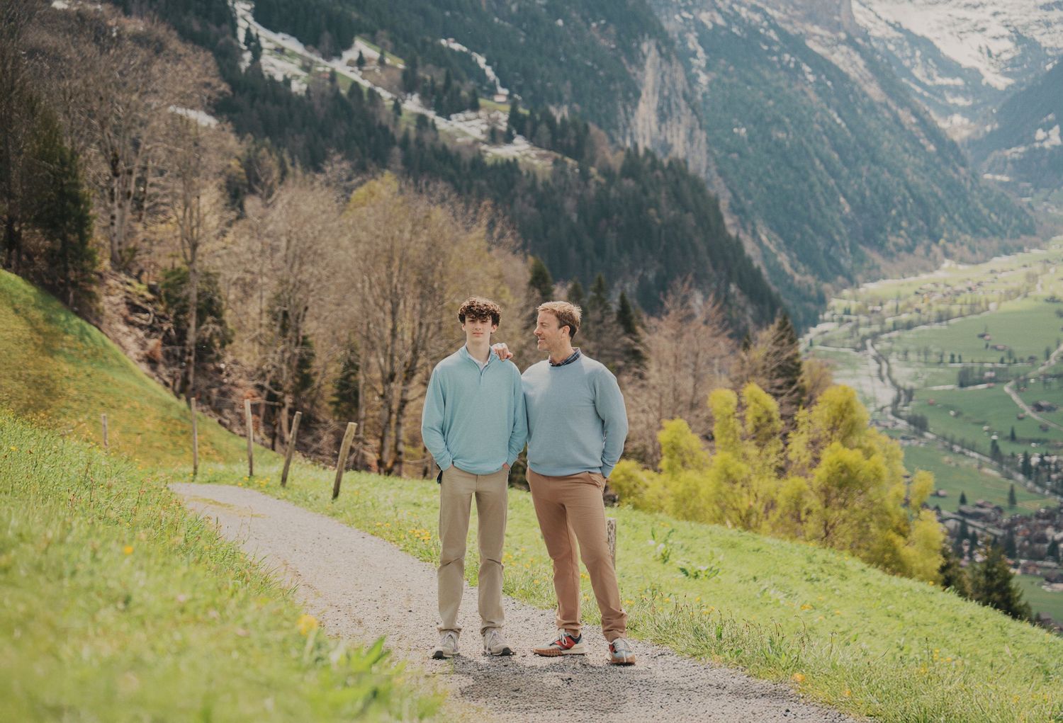 Two young men in matching blue sweaters standing on a mountain path in the Swiss Alps.