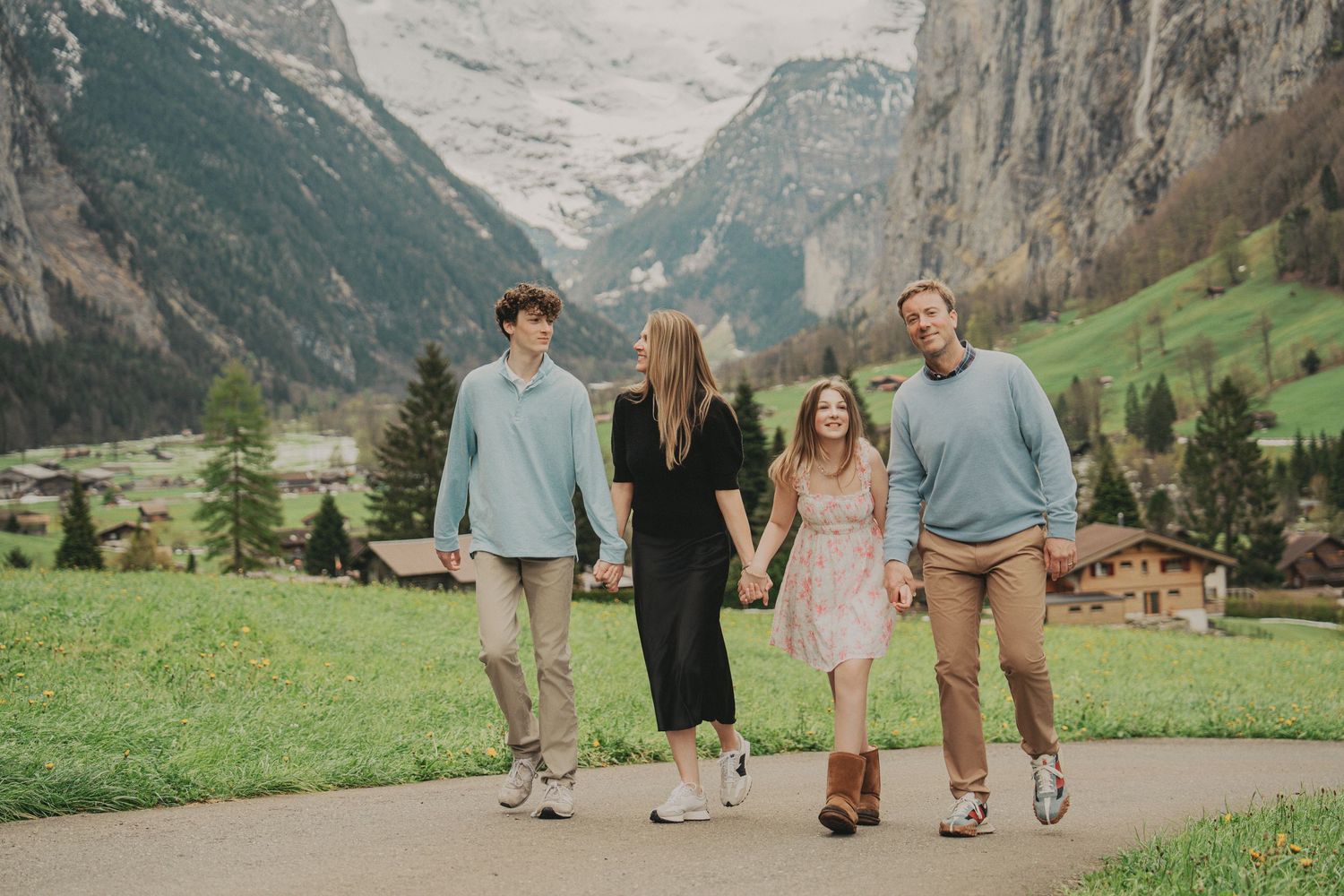 Family walking away on a scenic Swiss Alps path surrounded by green meadows and mountain views.