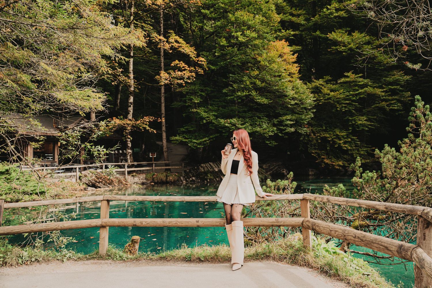 Young woman in white outfit standing on wooden bridge over stunning turquoise forest lake.