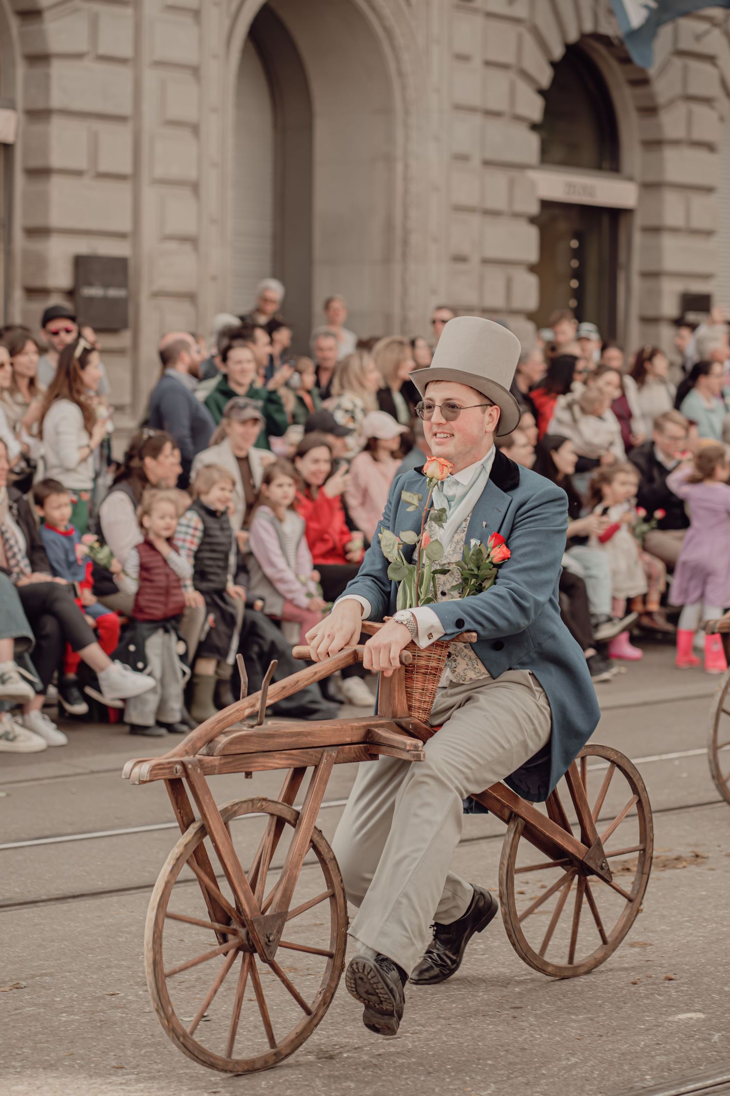 A man in vintage attire rides an antique wooden draisine bicycle during a colorful street parade.