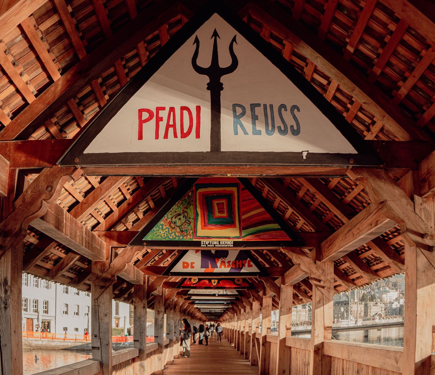 Wooden covered bridge interior decorated with colorful flags and Pfadi Reuss signage.