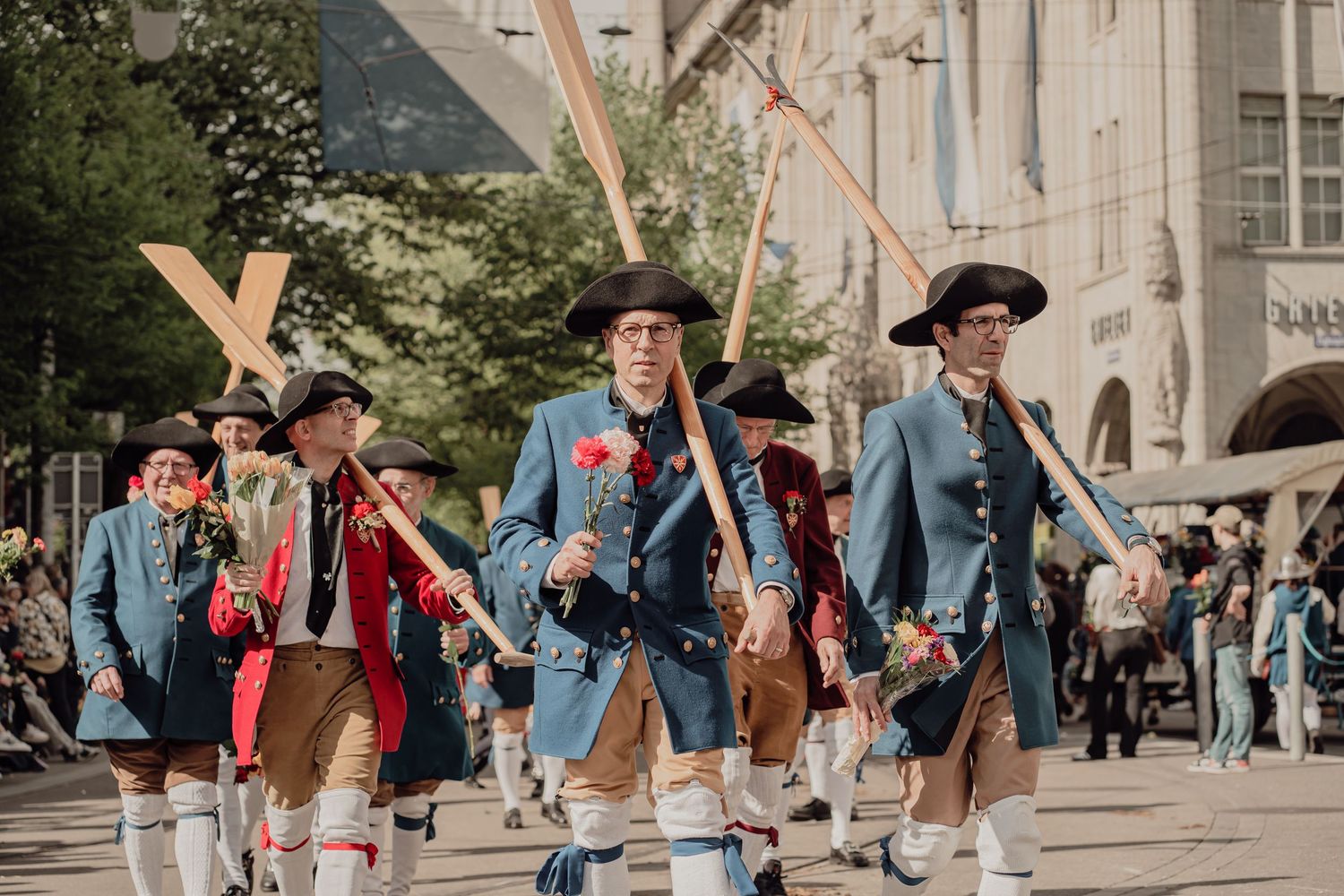 Men in historical blue Bavarian costumes march carrying wooden crosses in a traditional parade.