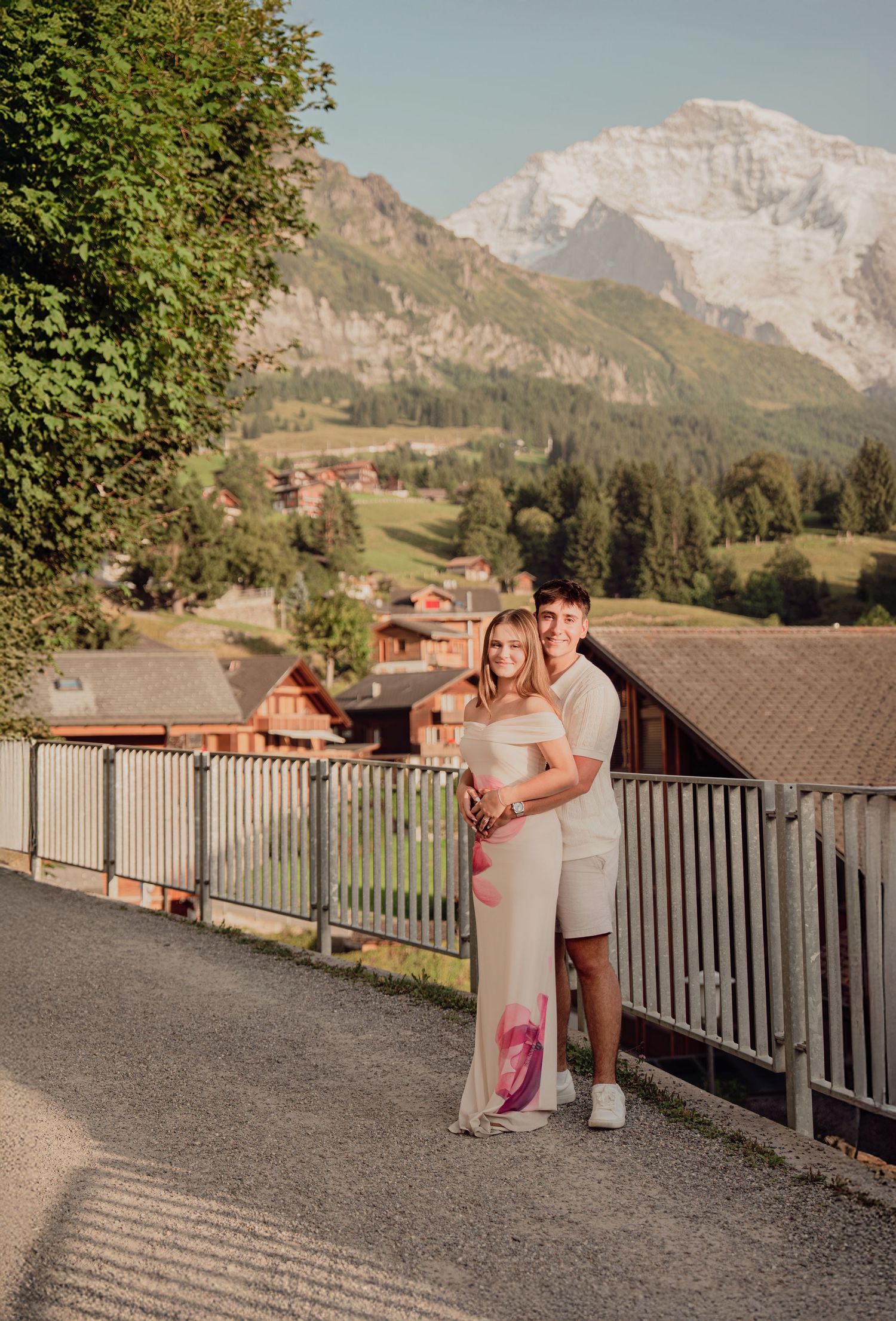 Couple embracing on a scenic alpine path with snow-capped mountains and green valley in Grindelwald, Switzerland.