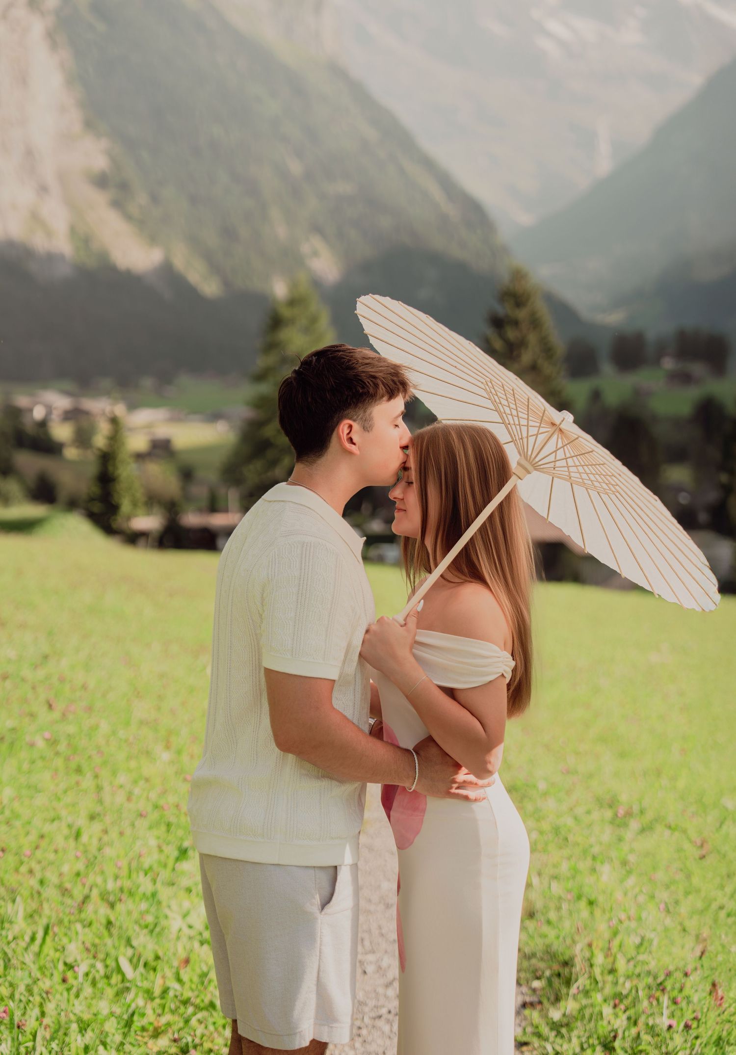 Couple sharing a kiss under a white parasol on a scenic alpine meadow path in Lauterbrunnen, Switzerland.