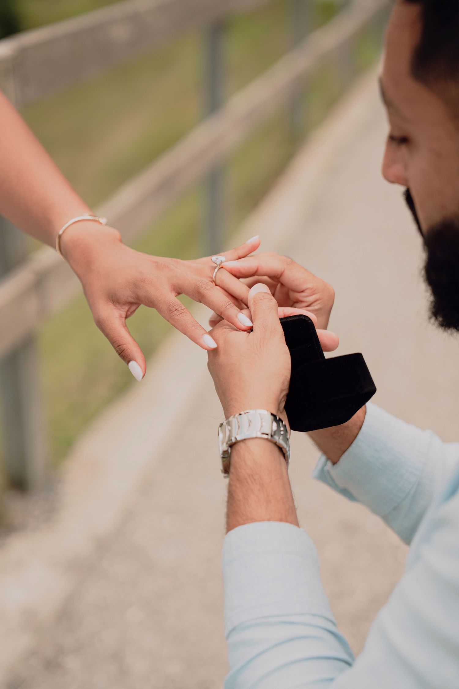 Man places diamond engagement ring on womans finger during a romantic outdoor proposal.