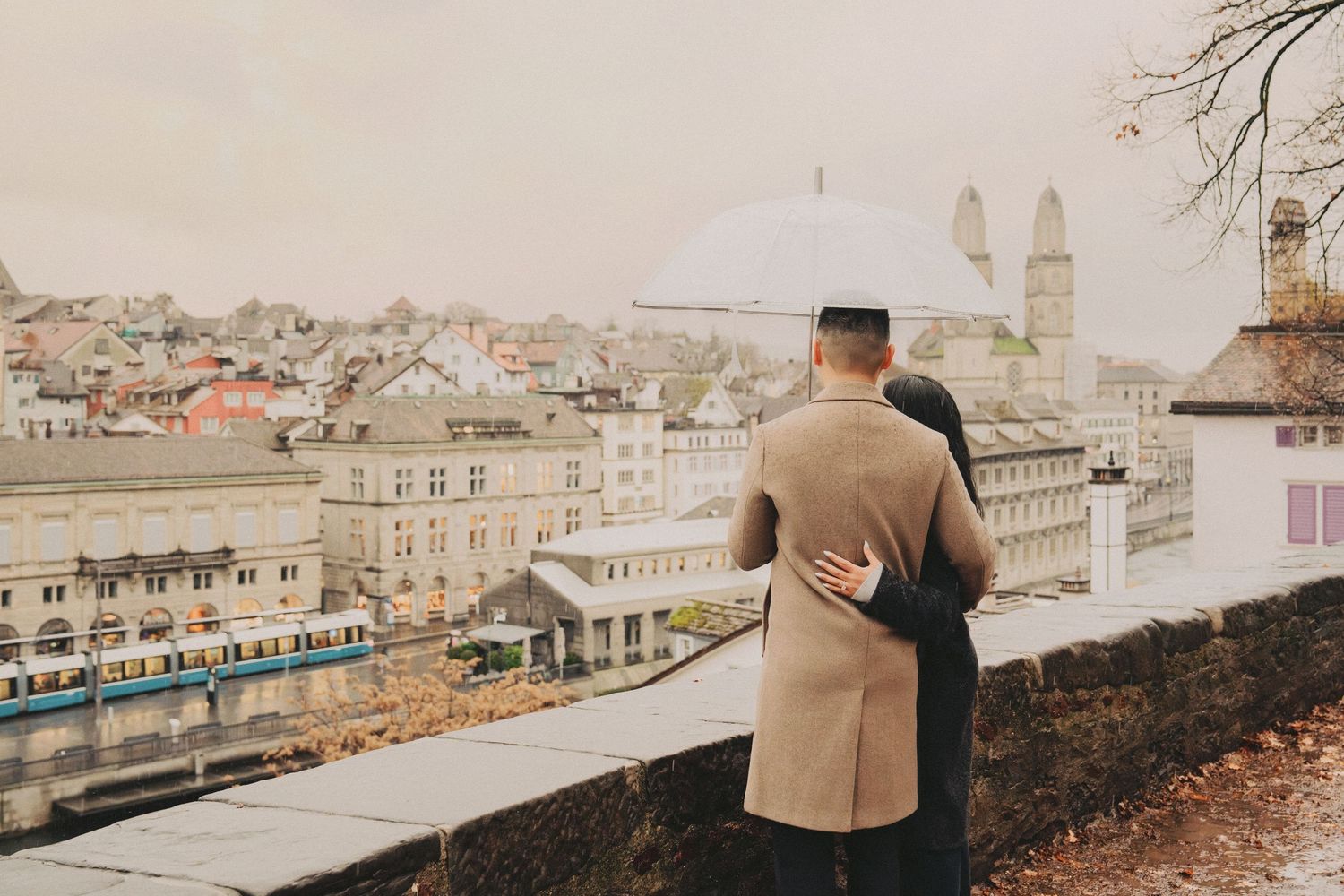 Couple hugging while overlooking the rainy Zurich skyline with historic church towers visible.