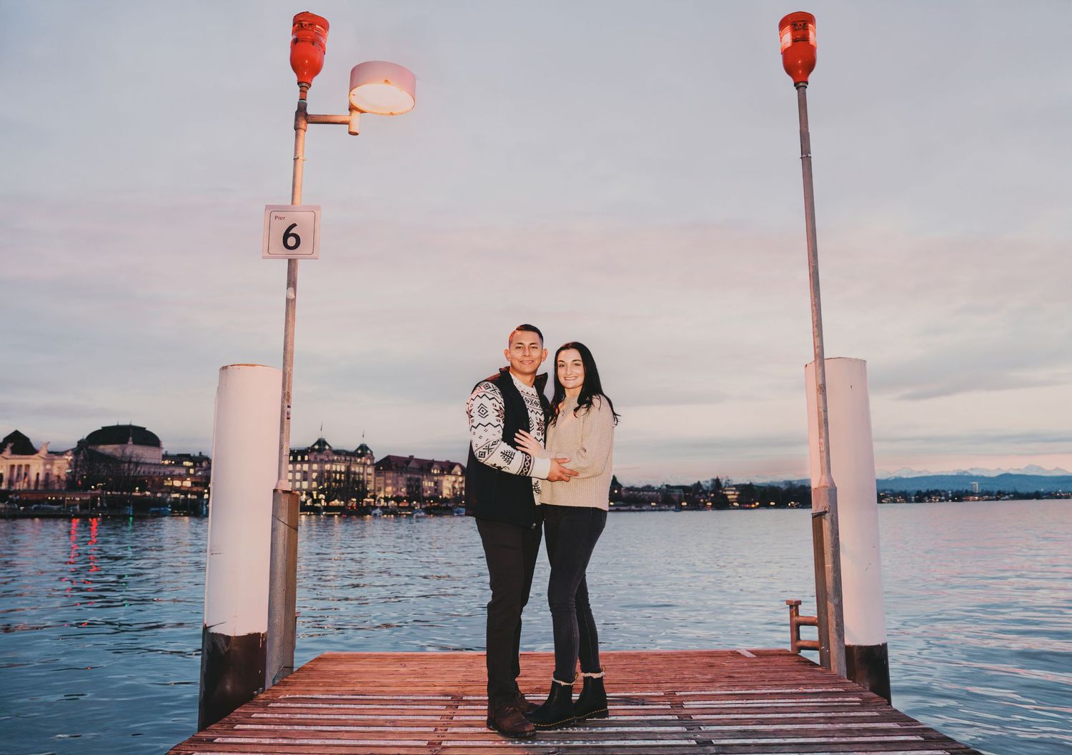 Happy couple standing close on a wooden pier by the lake during a pink sunset.