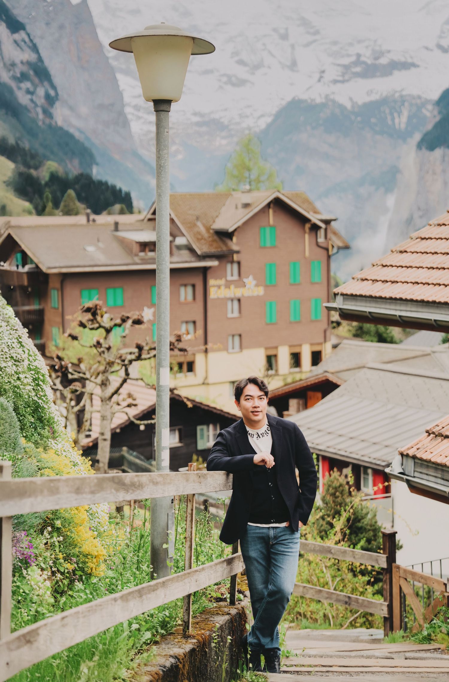 Young man in black blazer walking down wooden stairs in picturesque Alpine village.