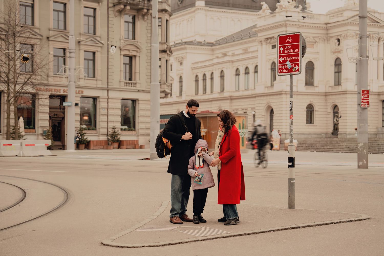 Family of three standing together on a city square with historic European architecture.