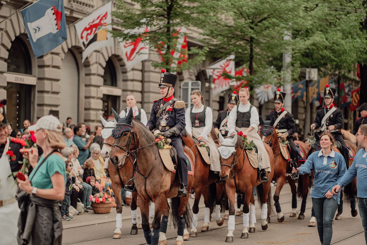 Riders in historic military and folk costumes parade on horseback through a crowded city street.