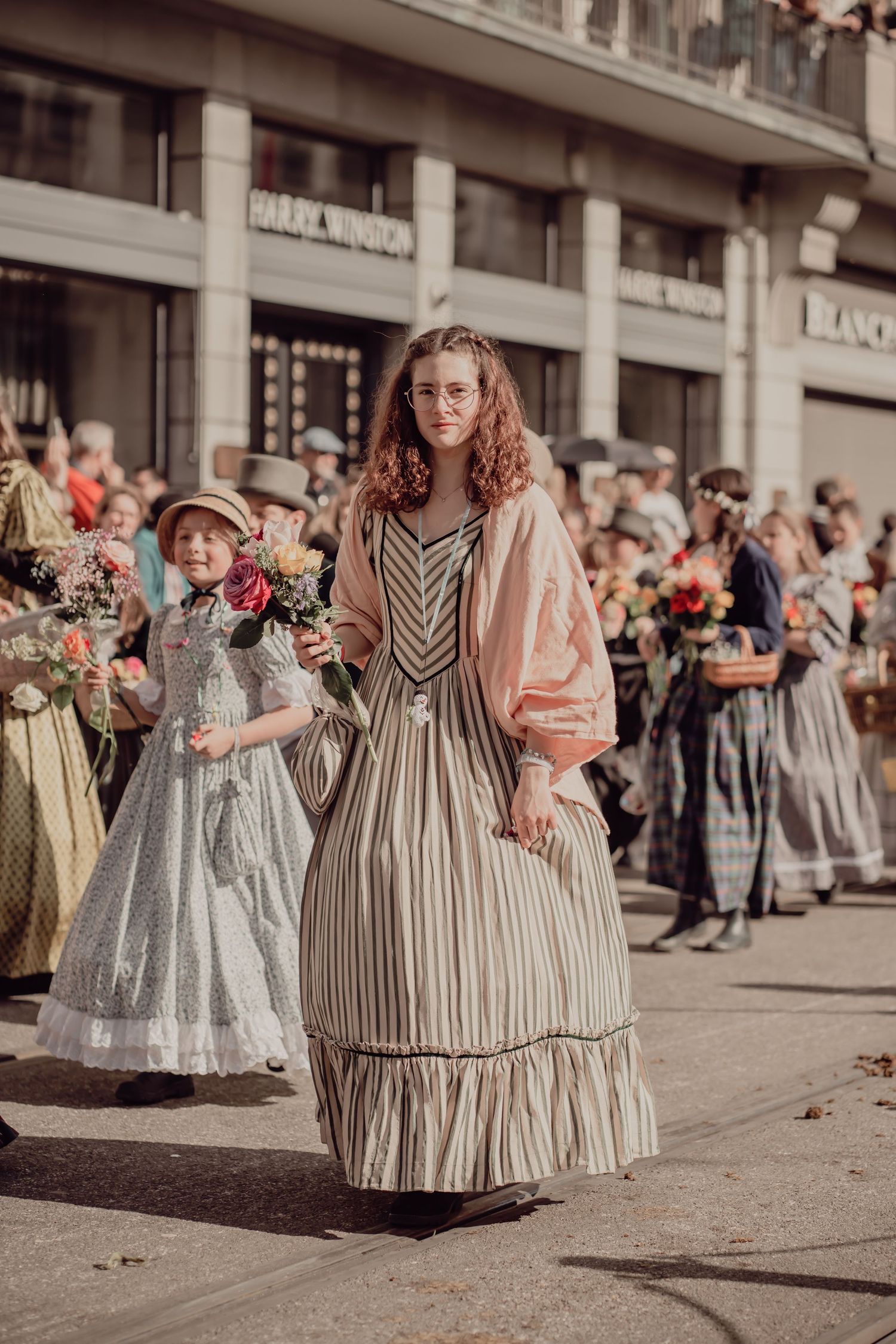 Young woman in a striped vintage dress walks with a child in a historical costume parade.