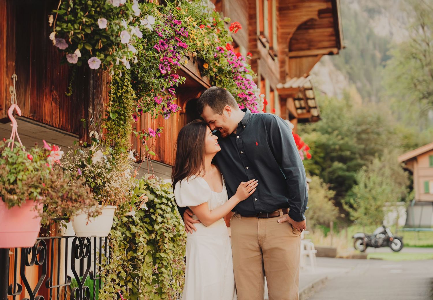 Romantic couple sharing a tender moment near a flower-adorned wooden chalet in the Swiss Alps.