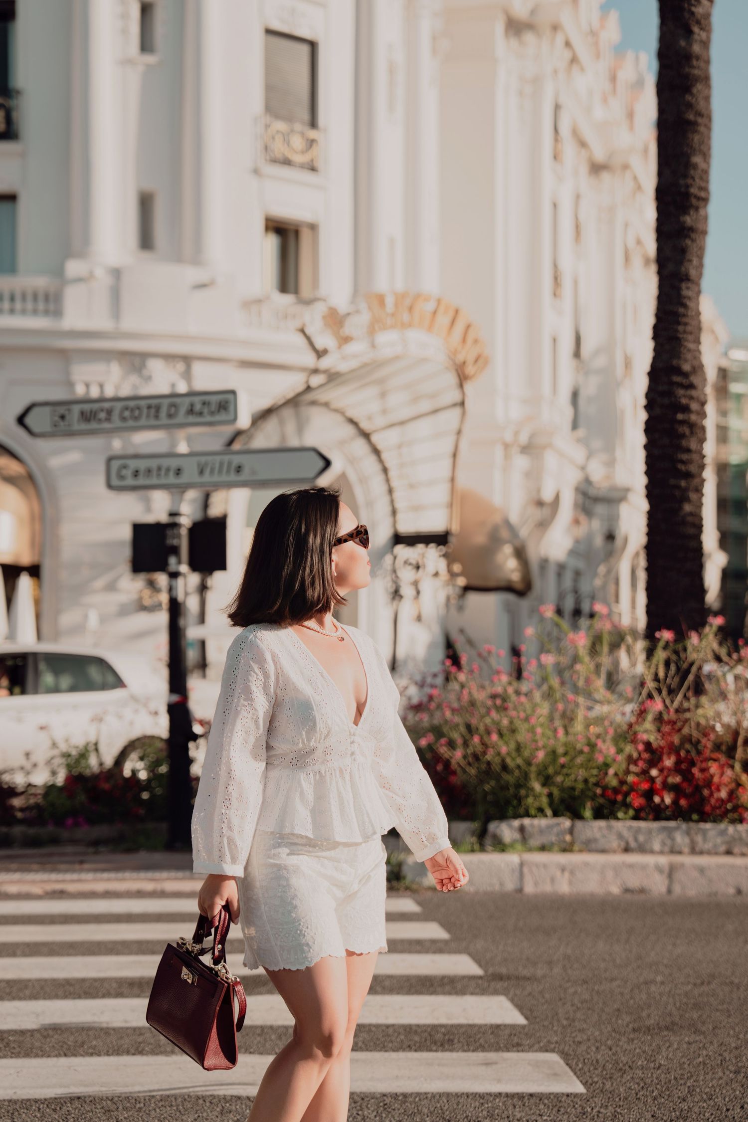 Chic woman in white lace outfit walking crosswalk near Nice Cote d Azur street sign.