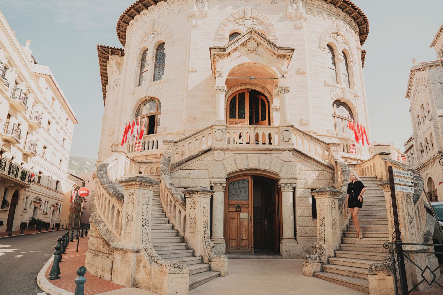 Historic Monaco courthouse with ornate stone staircase and red flags at entrance.