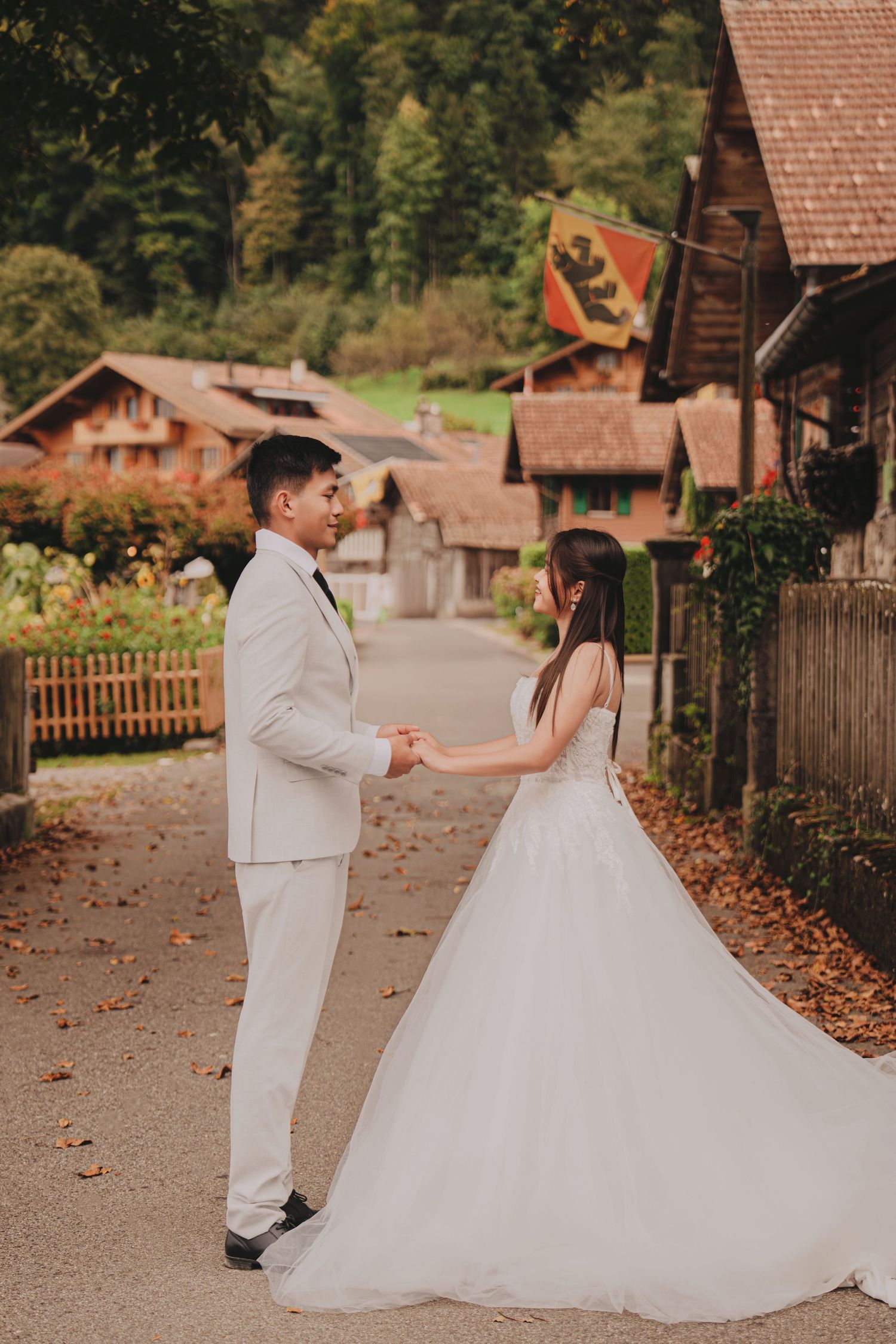 Wedding couple holding hands on a charming autumn village path surrounded by traditional Swiss wooden houses.